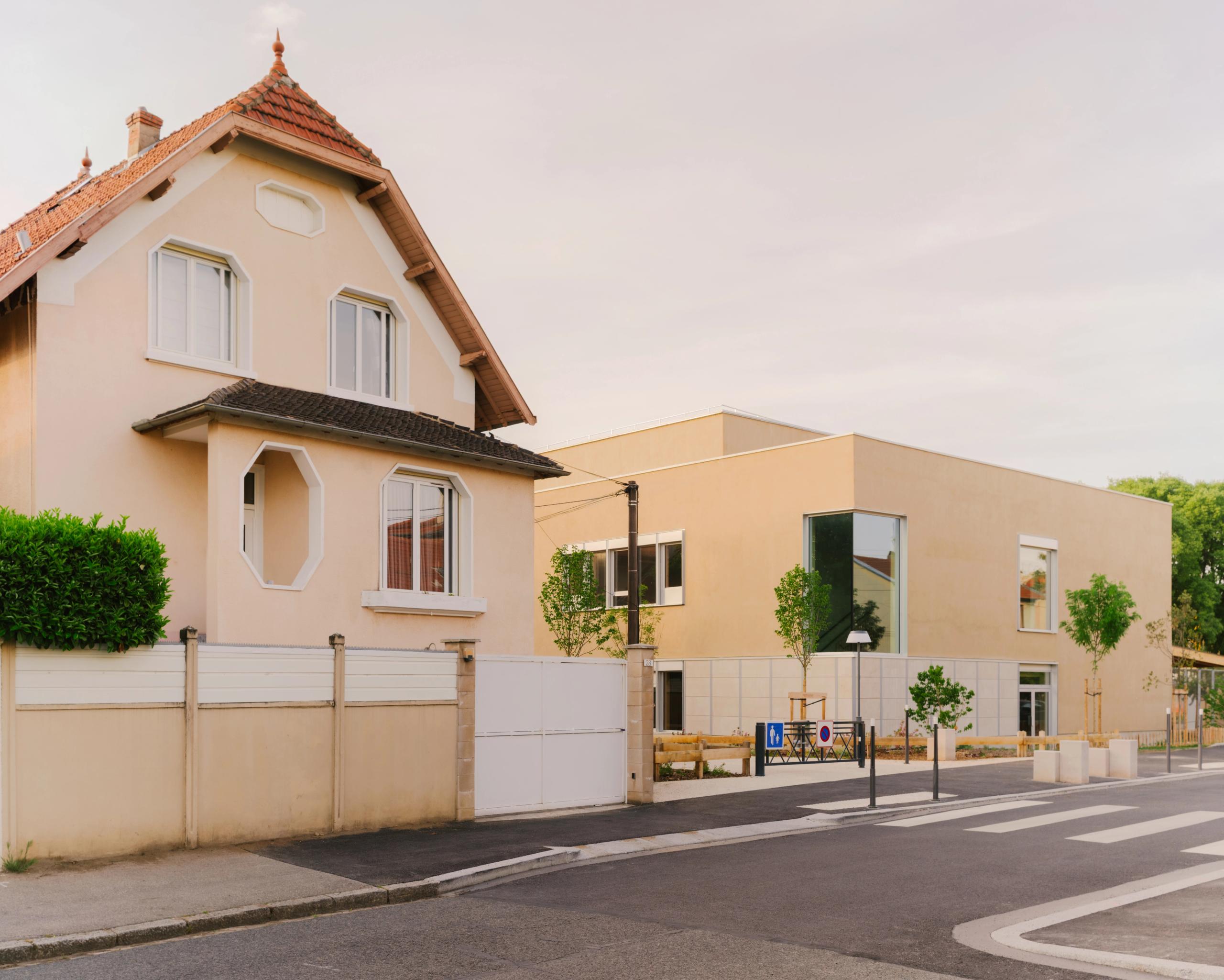 Vue de la façade du groupe scolaire Kennedy à Lyon, volume bois-paille enduit minéral en équerre, grandes baies vitrées sur cour végétalisée en cœur d’îlot.
