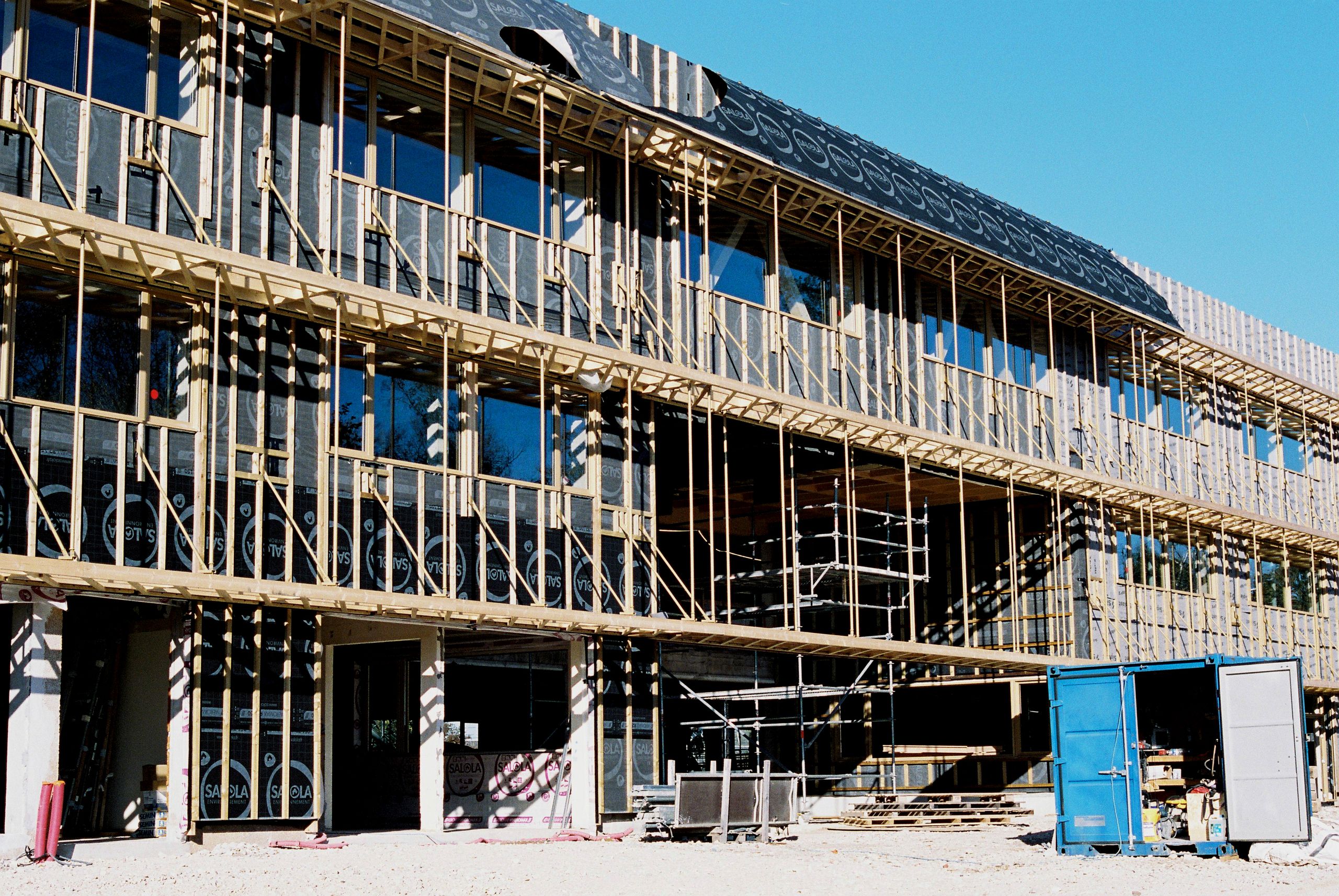 Chantier de restructuration du collège Maryse Bastié à Dole, façade en cours de surélévation avec ossature bois apparente, grandes baies vitrées et échafaudages.