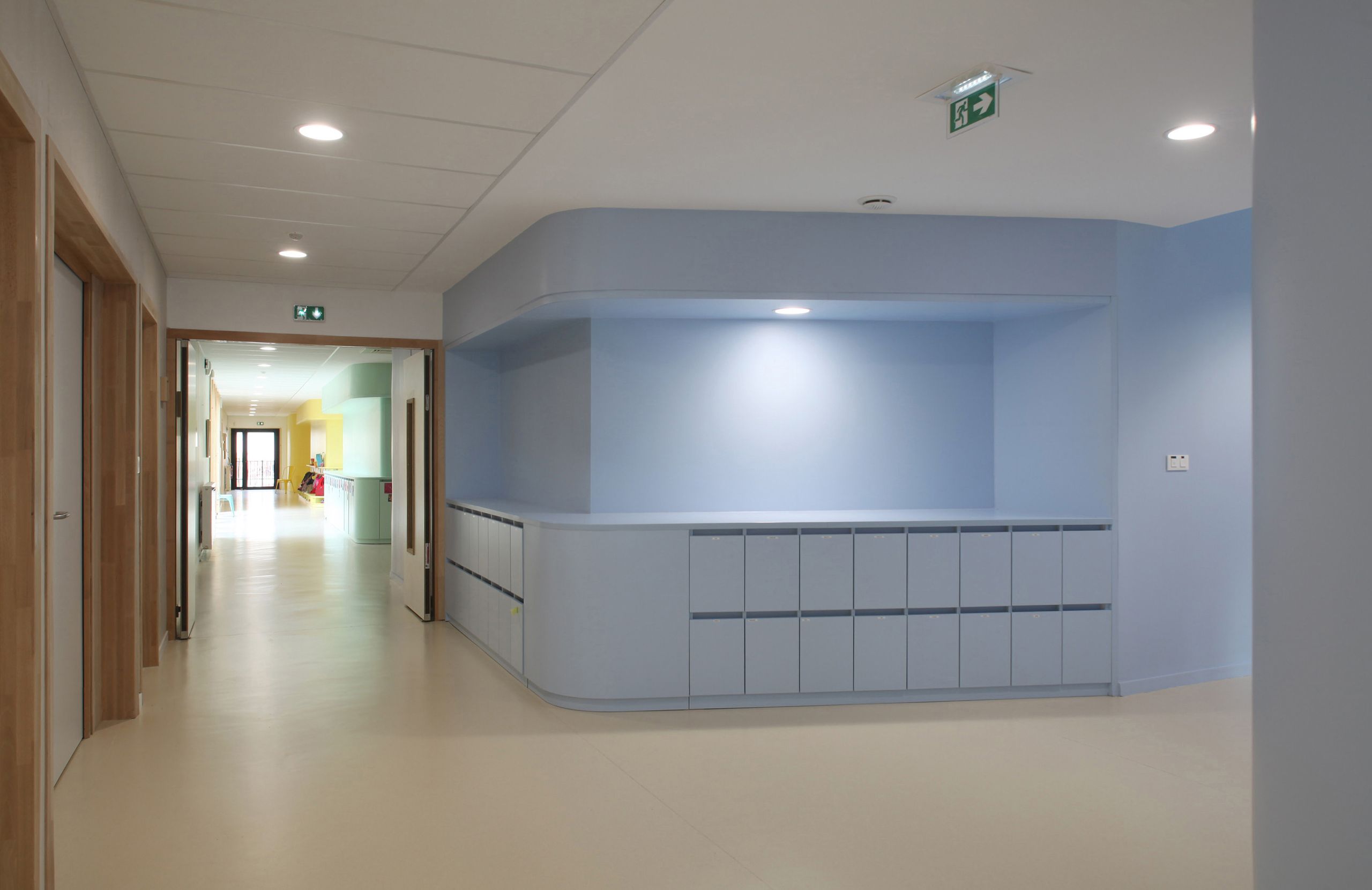 Galerie intérieure de la Maison de la petite enfance à Autun, avec mobilier intégré bleu aux angles arrondis, circulations claires et lumière naturelle en fond.