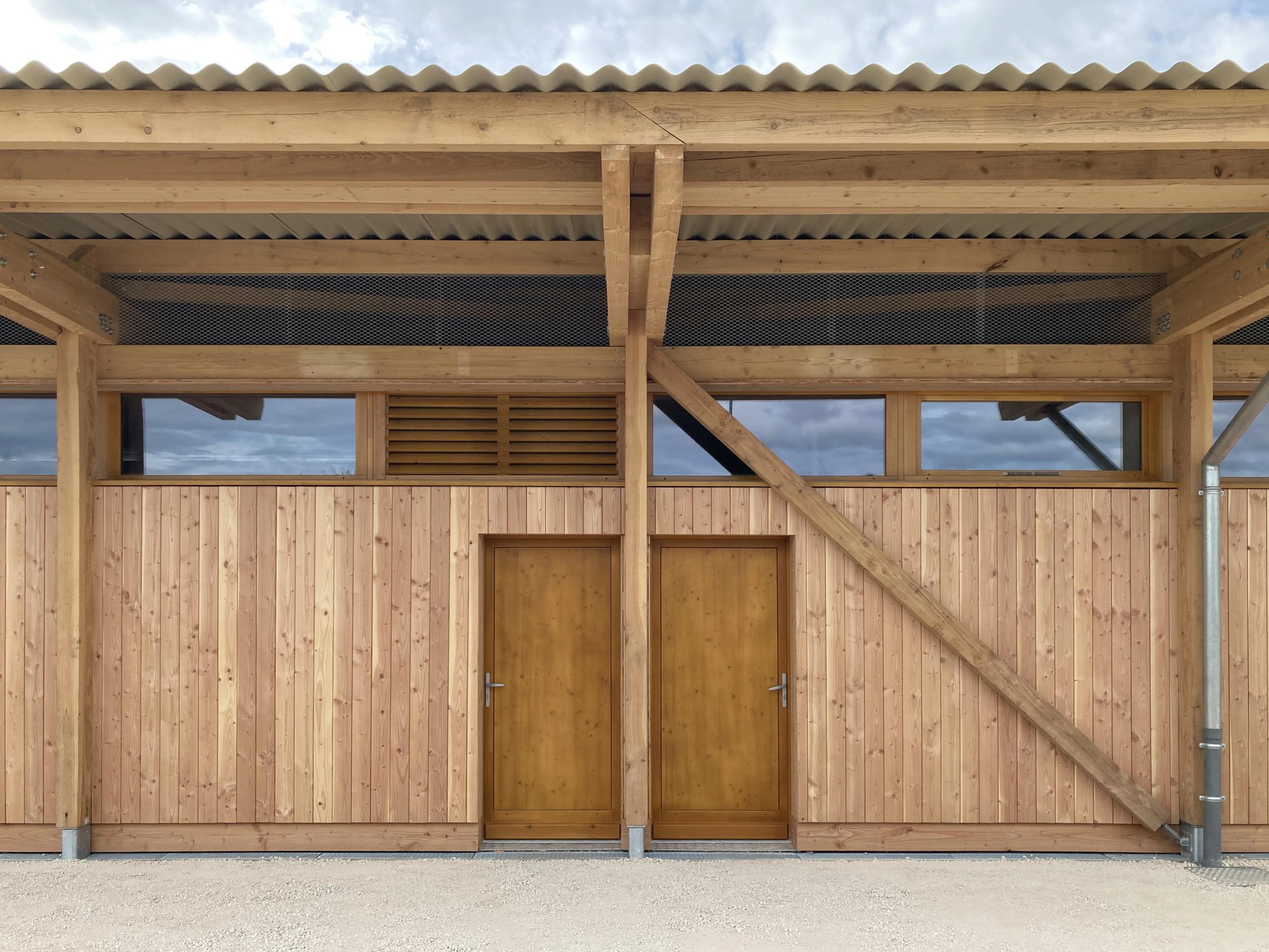 Façade en ossature bois de la Maison des sports à Malafretaz, bardage vertical, contreventement apparent, bande vitrée haute et couverture ondulée.