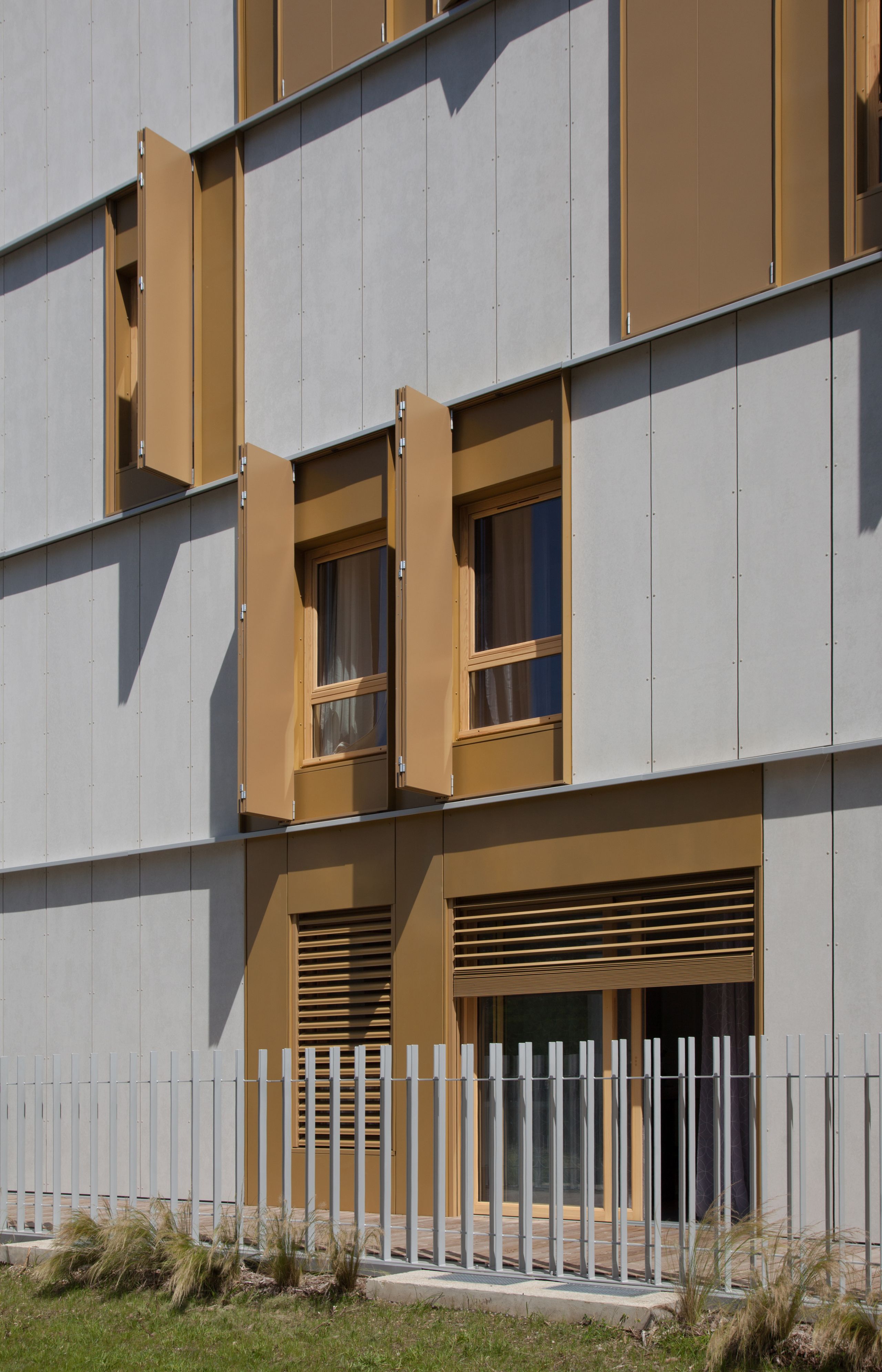 Façade des 55 logements à Lyon par Tectoniques, alternant panneaux béton clairs et menuiseries bois avec volets métalliques pivotants et protections solaires.