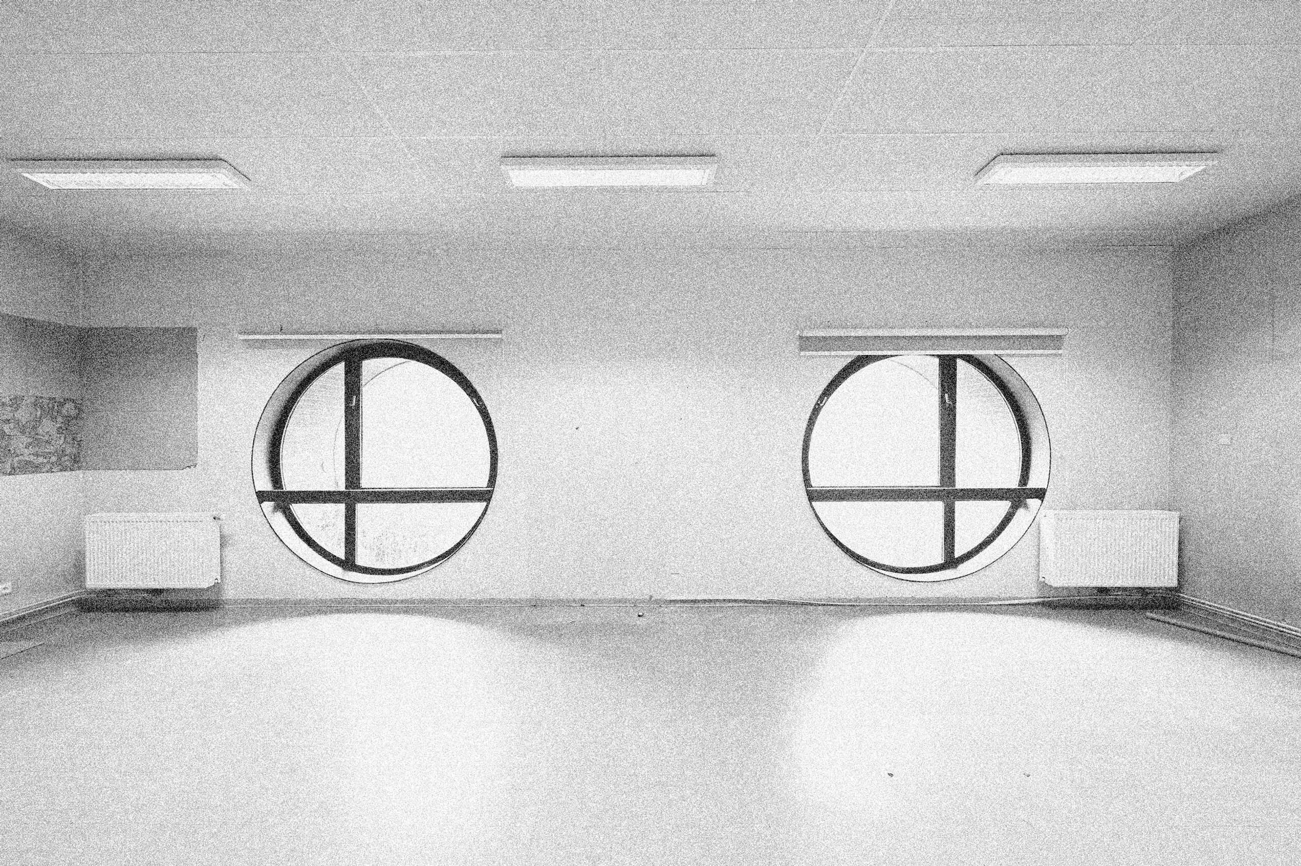 Vue intérieure du conservatoire d’Annemasse avant réhabilitation : salle nue éclairée par deux baies rondes à châssis métalliques et des plafonniers.