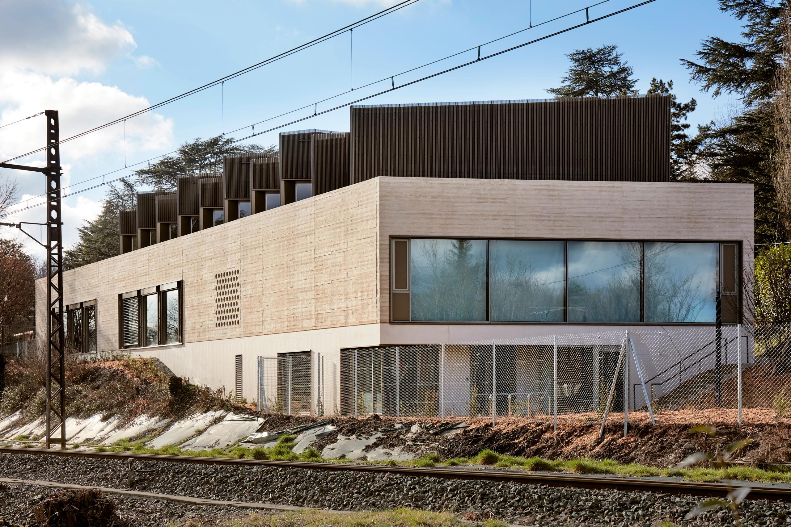 Maison des Arts à Charbonnières-les-Bains, volume en strates béton et couronnement bois-métal perforé, en lisière de voie ferrée dans un vallon arboré.