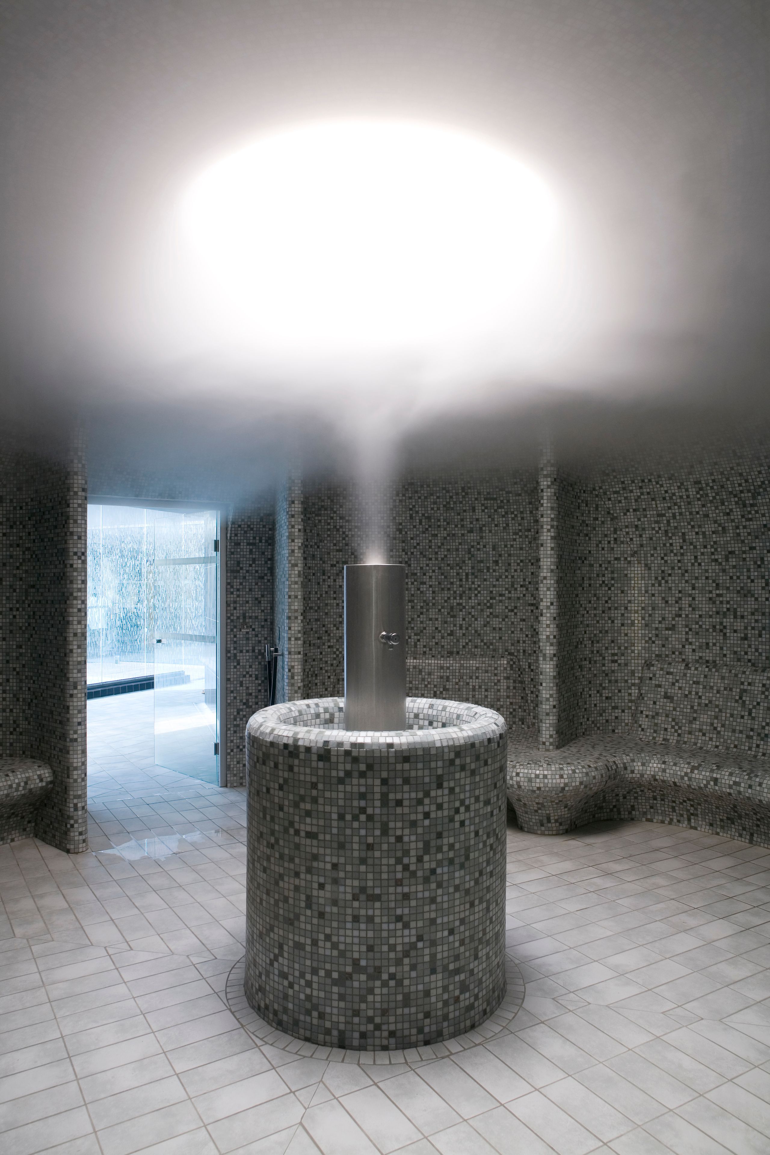 Espace vapeur du centre thermal de Balaruc-les-Bains, bassin circulaire carrelé et colonne inox diffusant la brume, ouvert sur les bassins extérieurs vitrés.