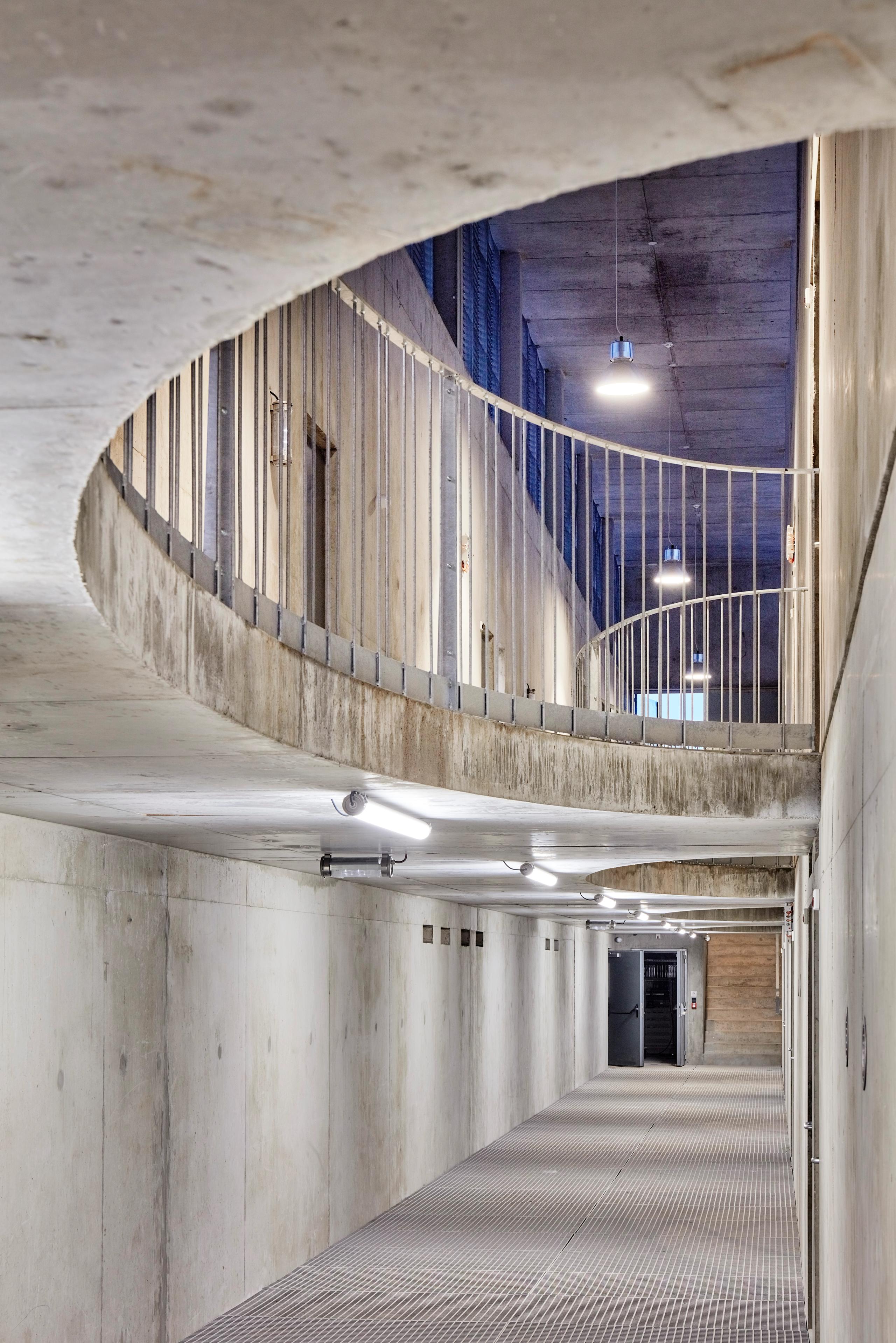 Circulation en triple hauteur du poste source de Cusset à Villeurbanne, couloir technique en béton brut, garde-corps métalliques et éclairage industriel.