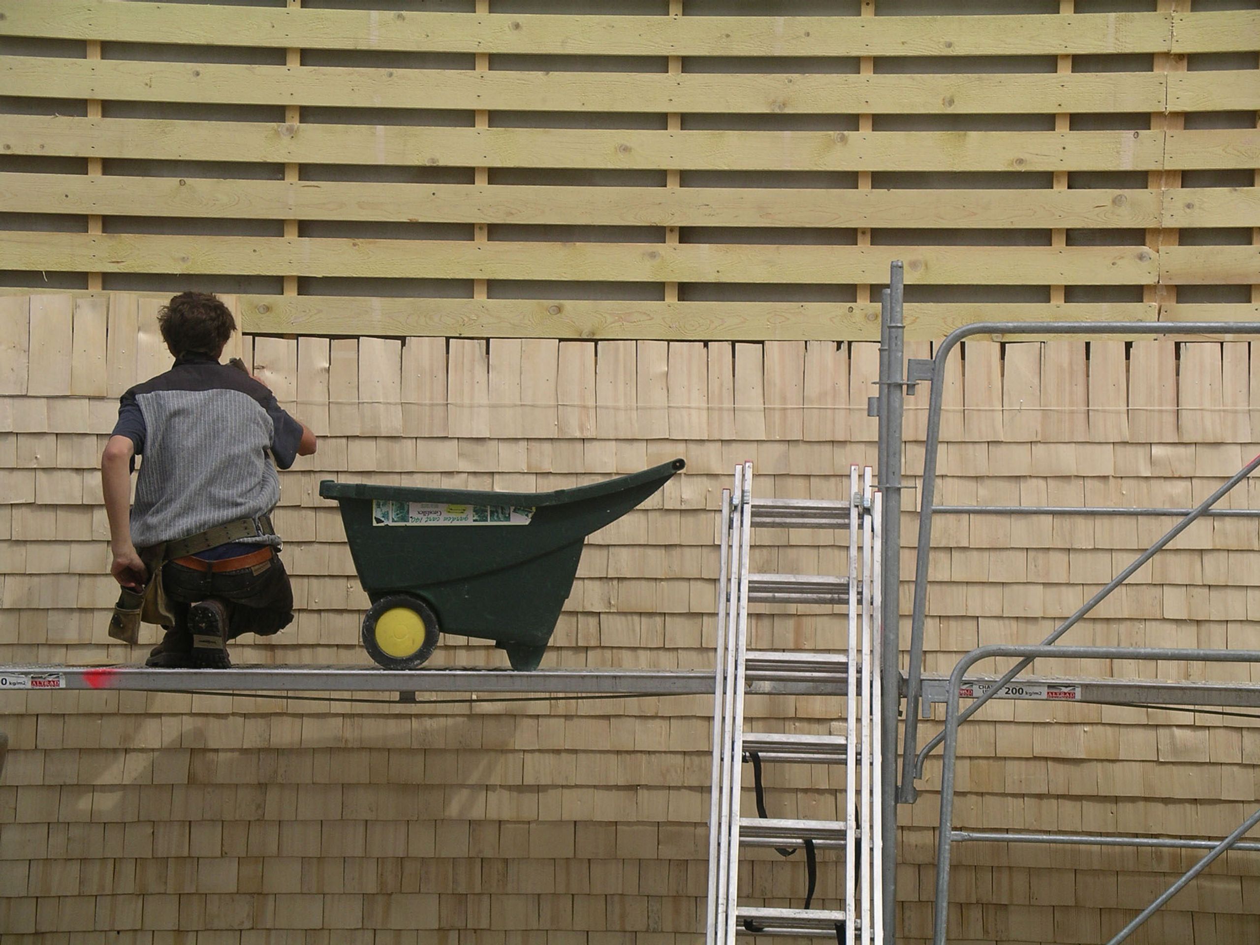 Pose du bardage en tavaillons d’épicéa sur la façade de la Maison du Parc du Haut-Jura à Lajoux, vue rapprochée du chantier et de l’échafaudage.