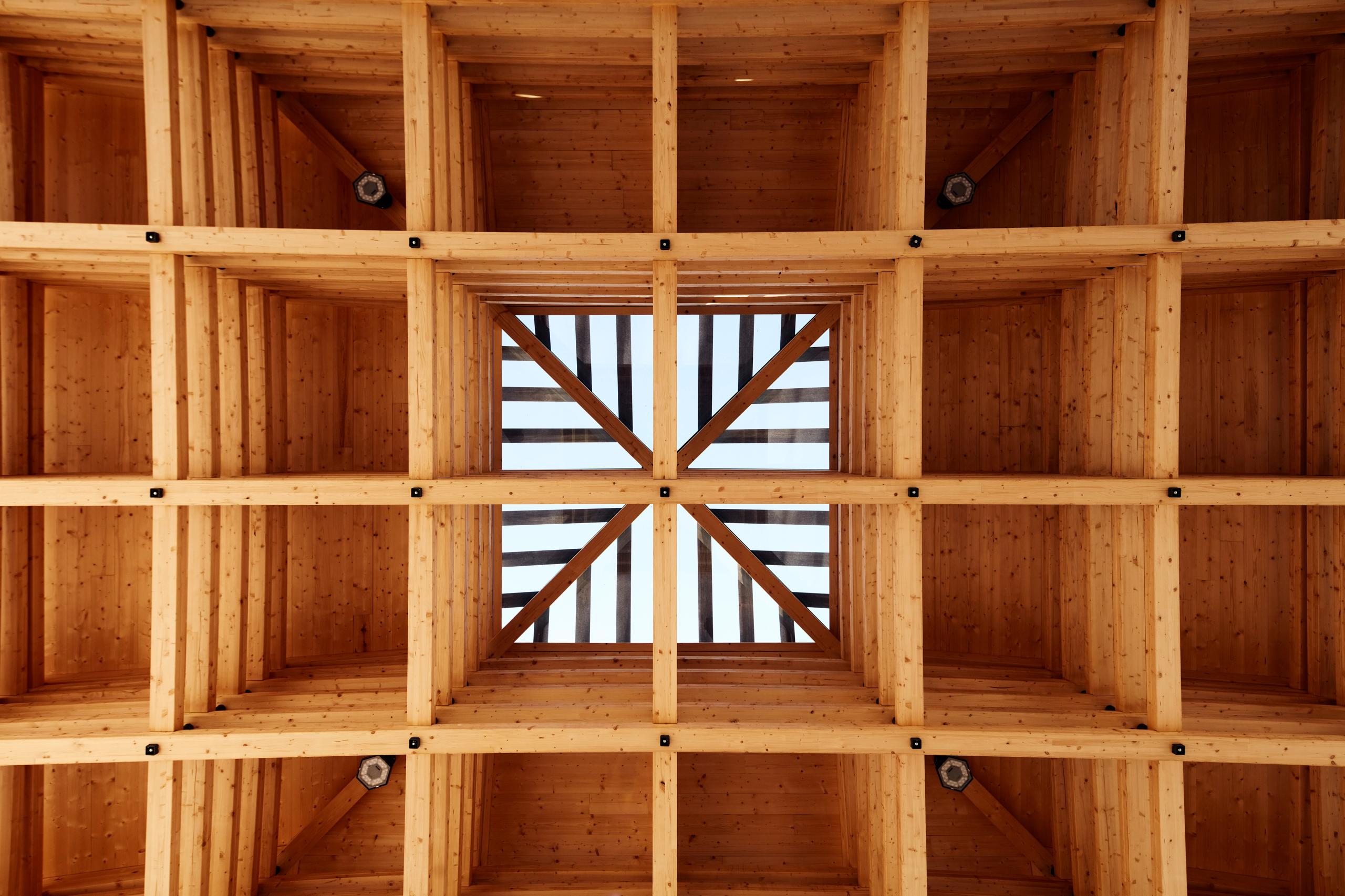 Sous-face de la halle de marché de Marcy-l’Étoile par Tectoniques, montrant la charpente en lamellé-collé formant une grille tridimensionnelle avec lanterneau central.