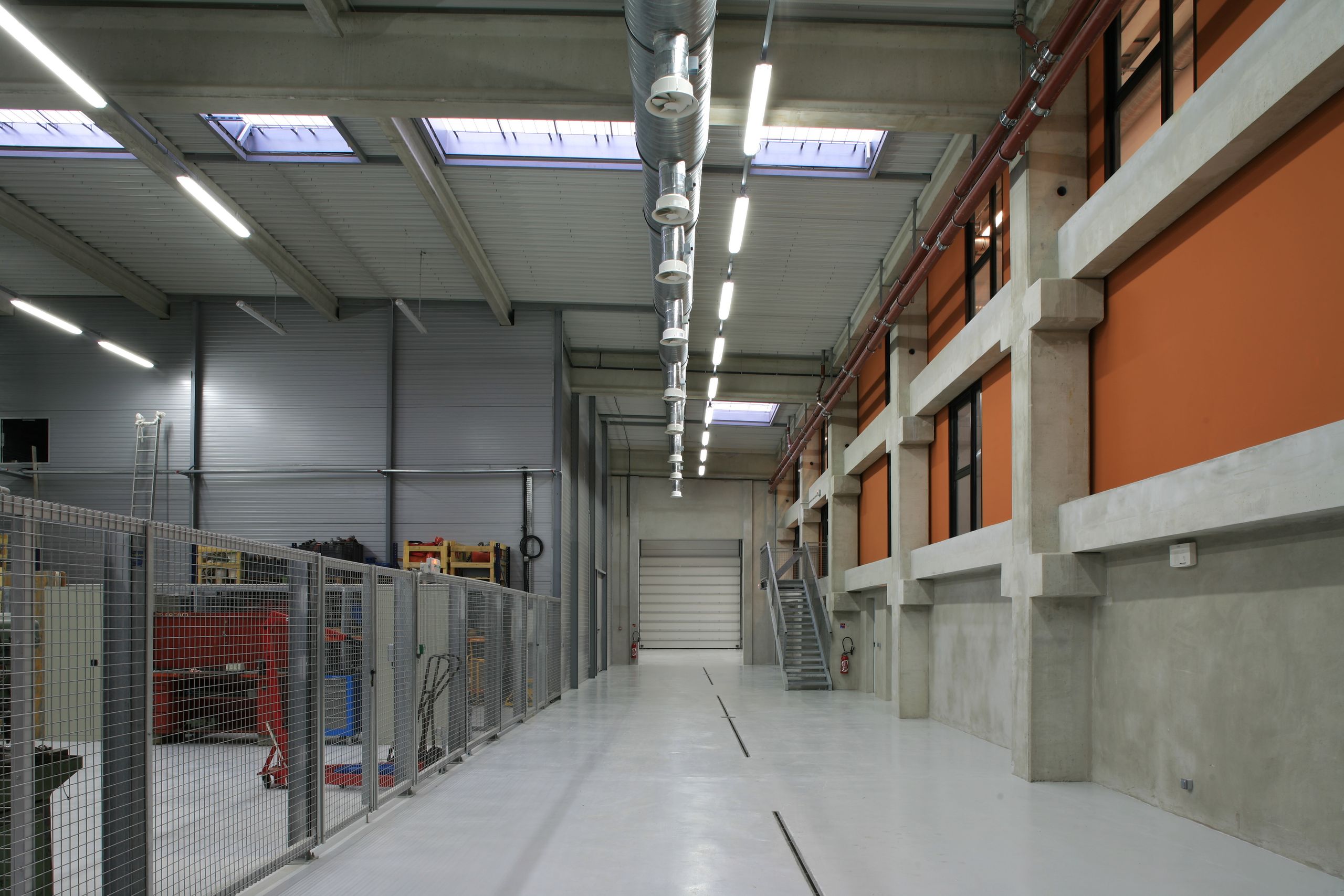 Grand hall technique du Département des Recherches Subaquatiques et Sous-Marines à Marseille, structure béton, façades intérieures orange, sheds et gaines apparentes.