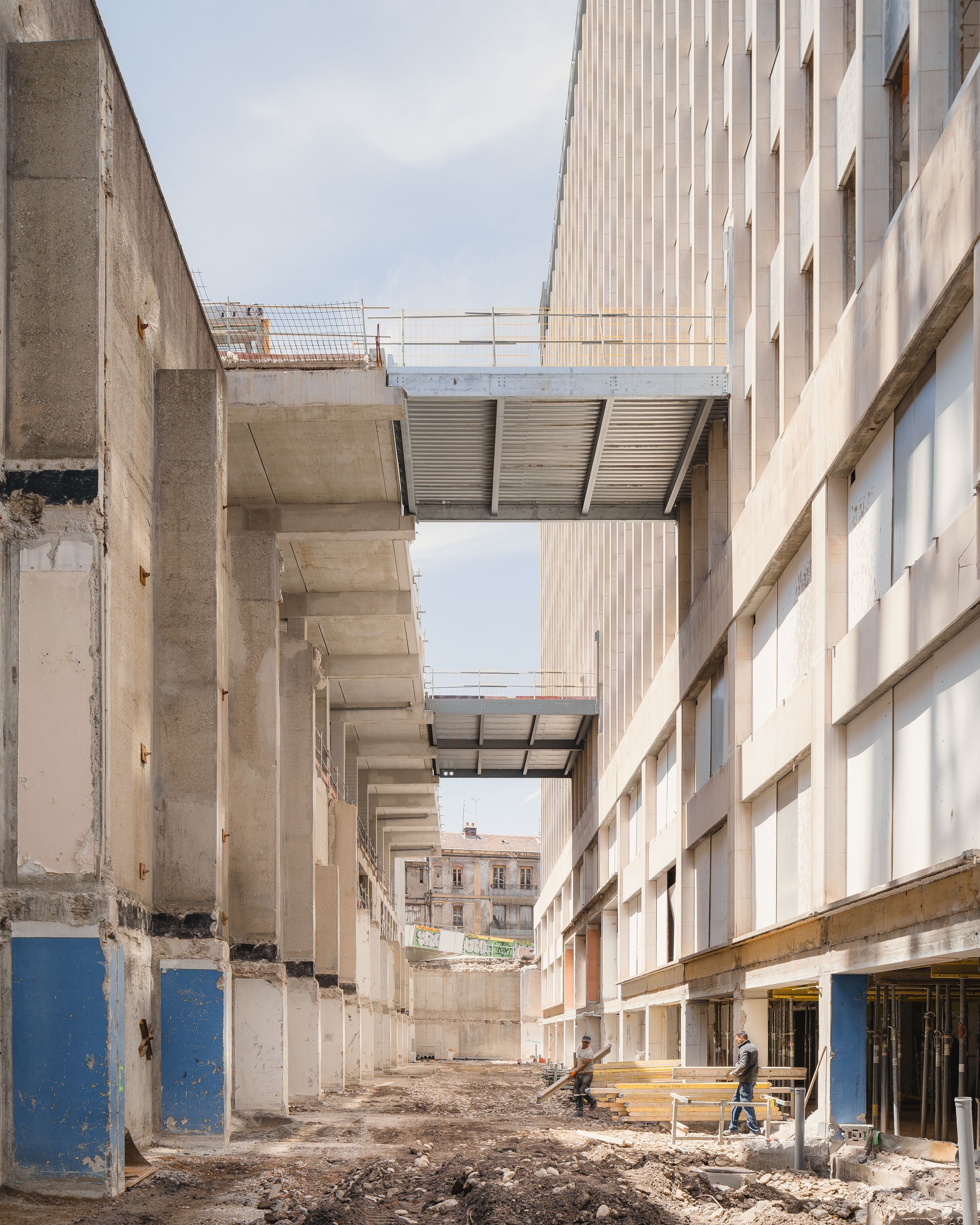 Chantier de réhabilitation de l’IGH Émile Loubet à Saint-Étienne, socle évidé en béton brut, passerelles métalliques et façades administratives des années 1970.