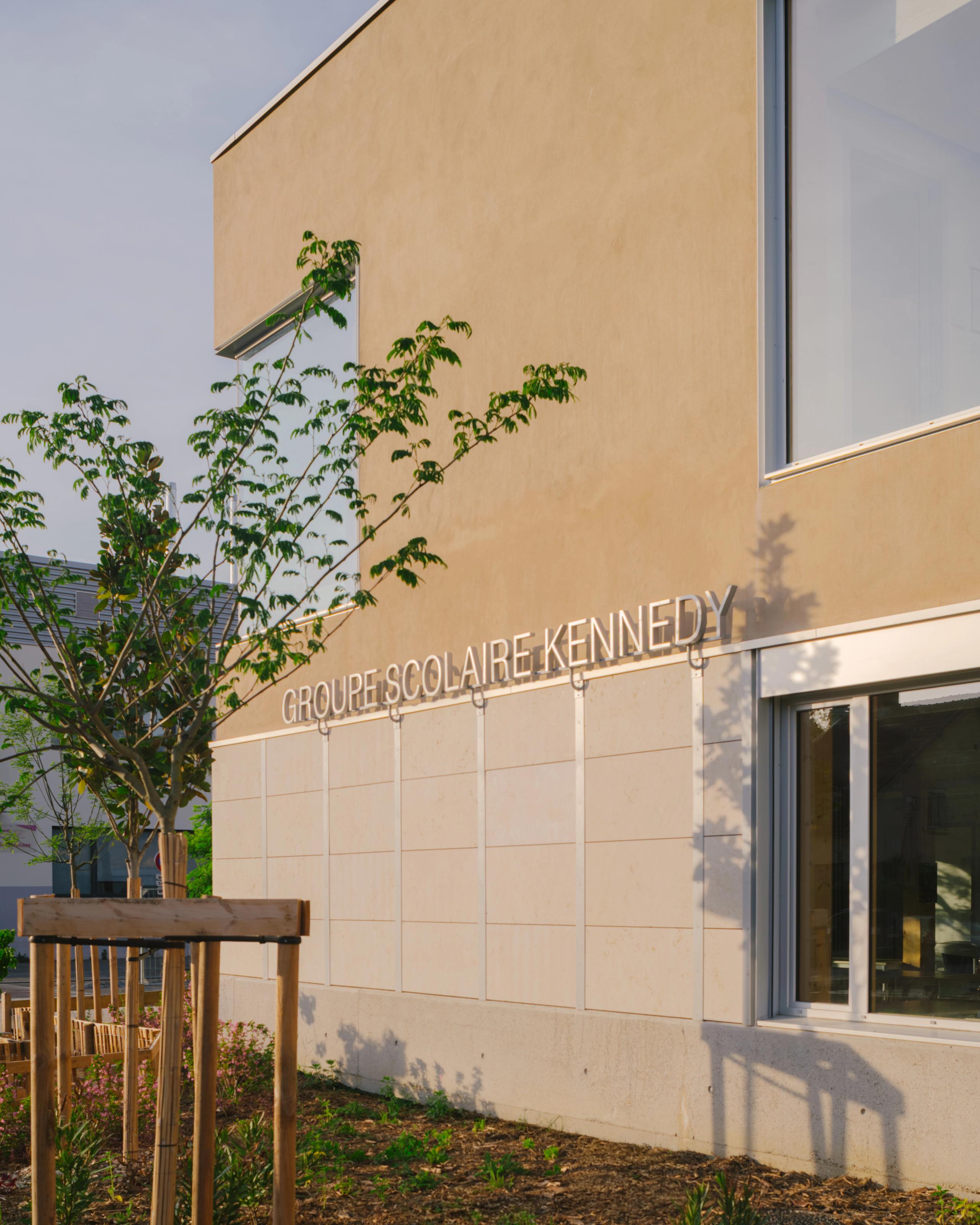 Façade minérale du Groupe scolaire Kennedy à Lyon, volume simple enduit clair, grandes baies vitrées et jardin planté en pied de bâtiment.