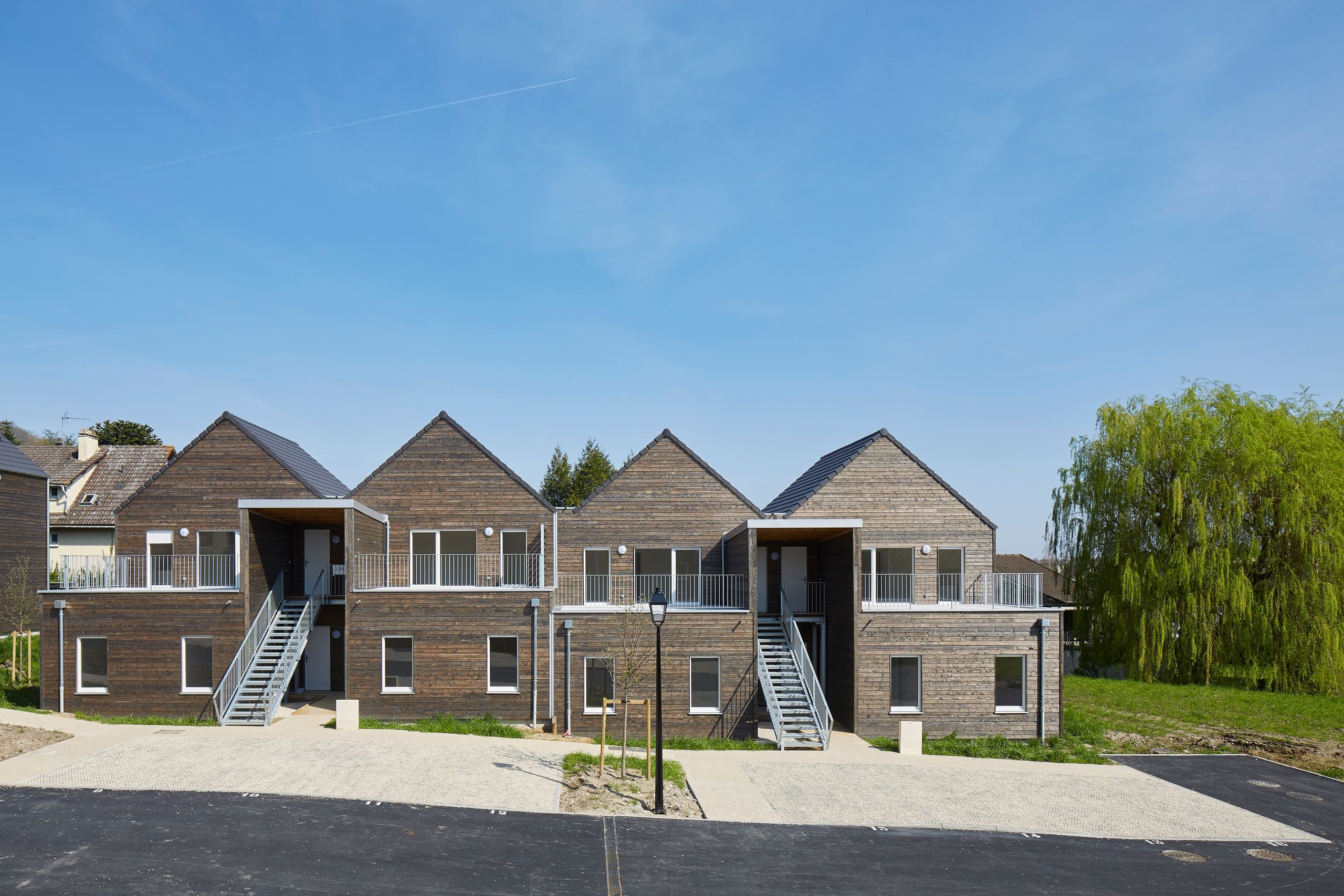 Vue de la résidence Tectoniques, 36 logements à Vauhallan : volumes en bois à toitures à deux pans, circulations extérieures et escaliers métalliques sur cour minérale.