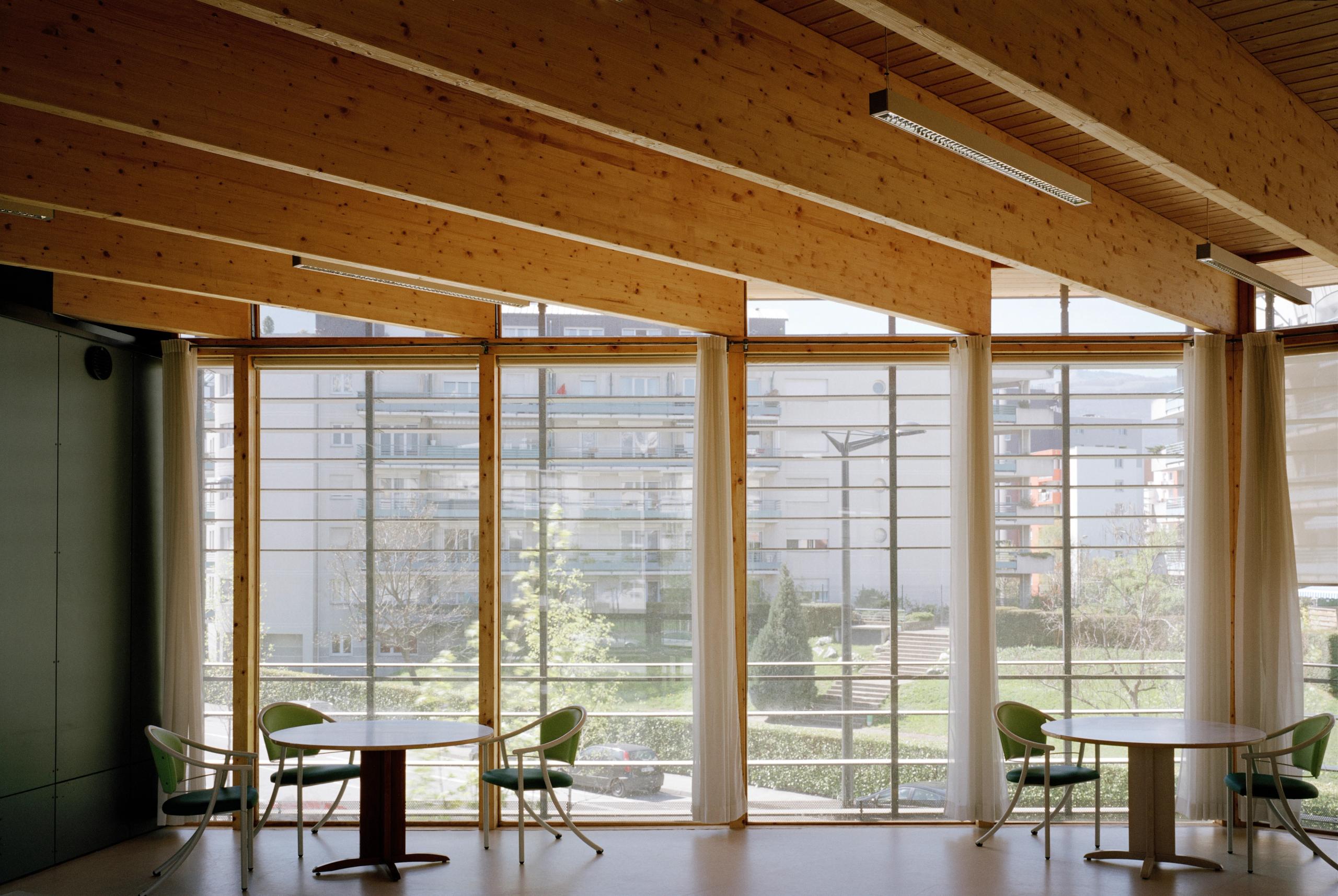 Espace commun de l’EHPAD à Grenoble par Tectoniques, avec structure bois apparente, larges baies vitrées sur jardins et mobilier sobre pour les résidents.