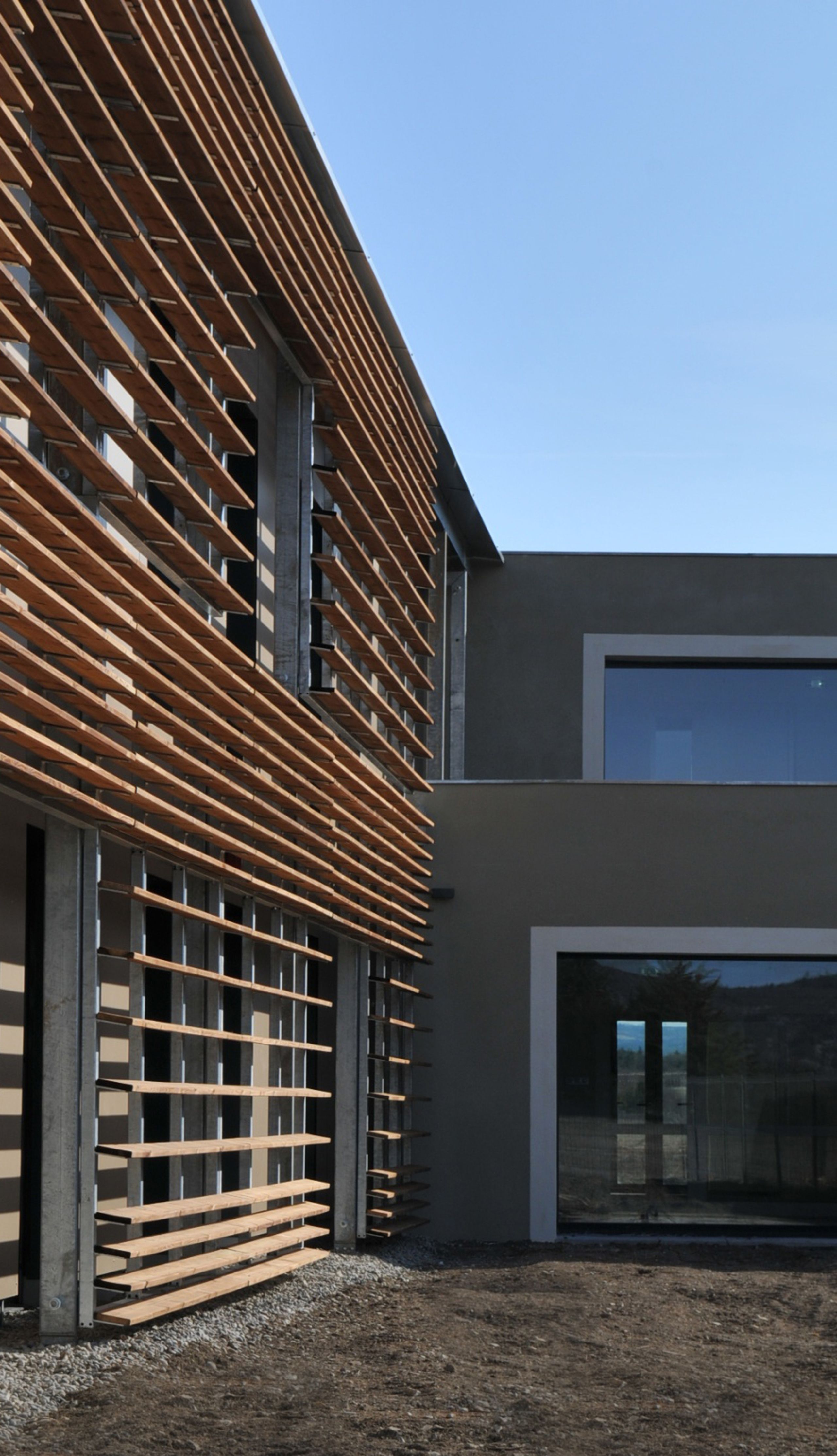 Façade de l’EHPAD de Sault par Tectoniques, volumes en H enduits gris, grandes baies vitrées et brise-soleil horizontaux en bois ouvrant sur le paysage.