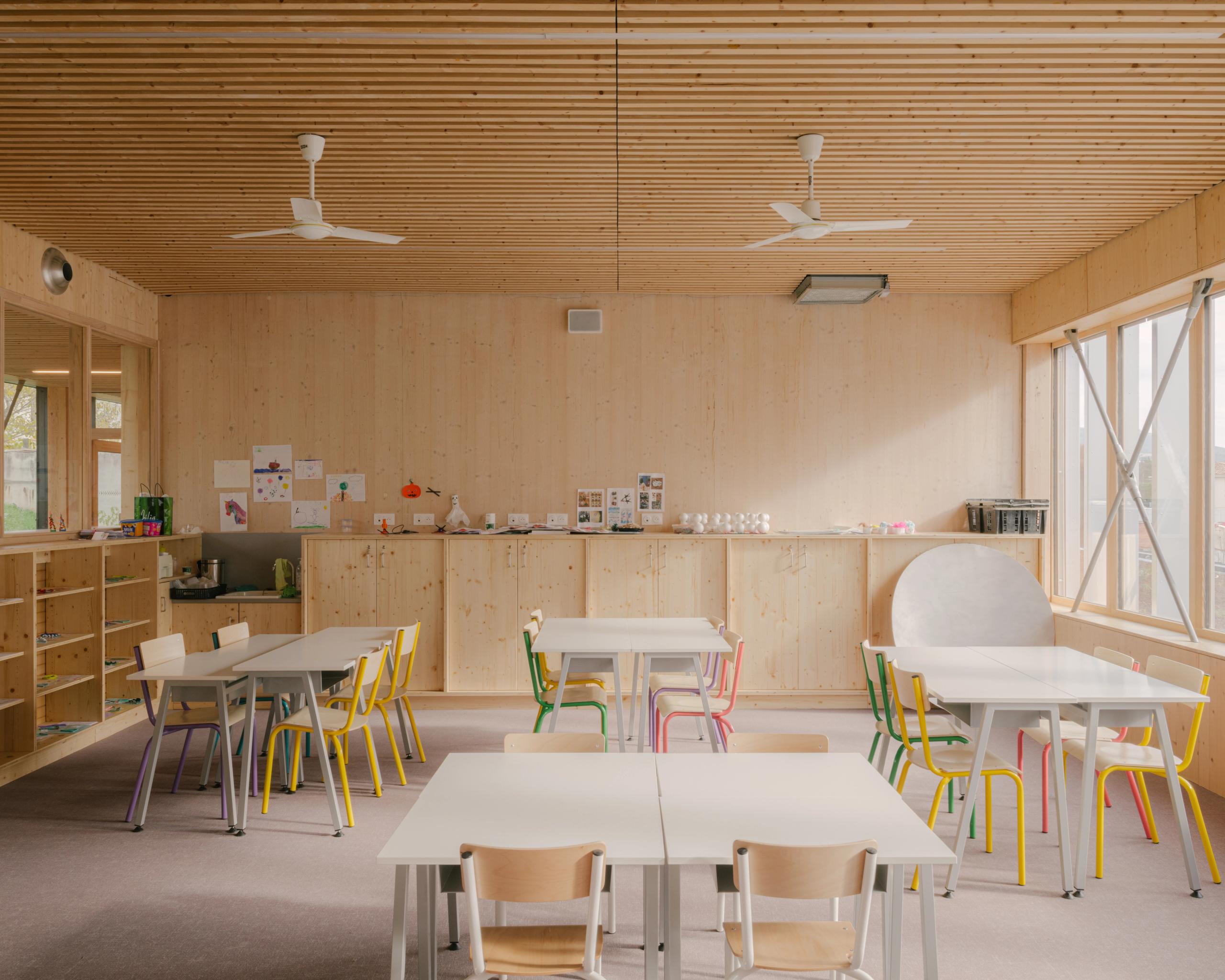 Salle de classe du groupe scolaire Claudie Haigneré aux Pennes-Mirabeau, structure bois apparente, plafond à lames, lumière naturelle et mobilier coloré.