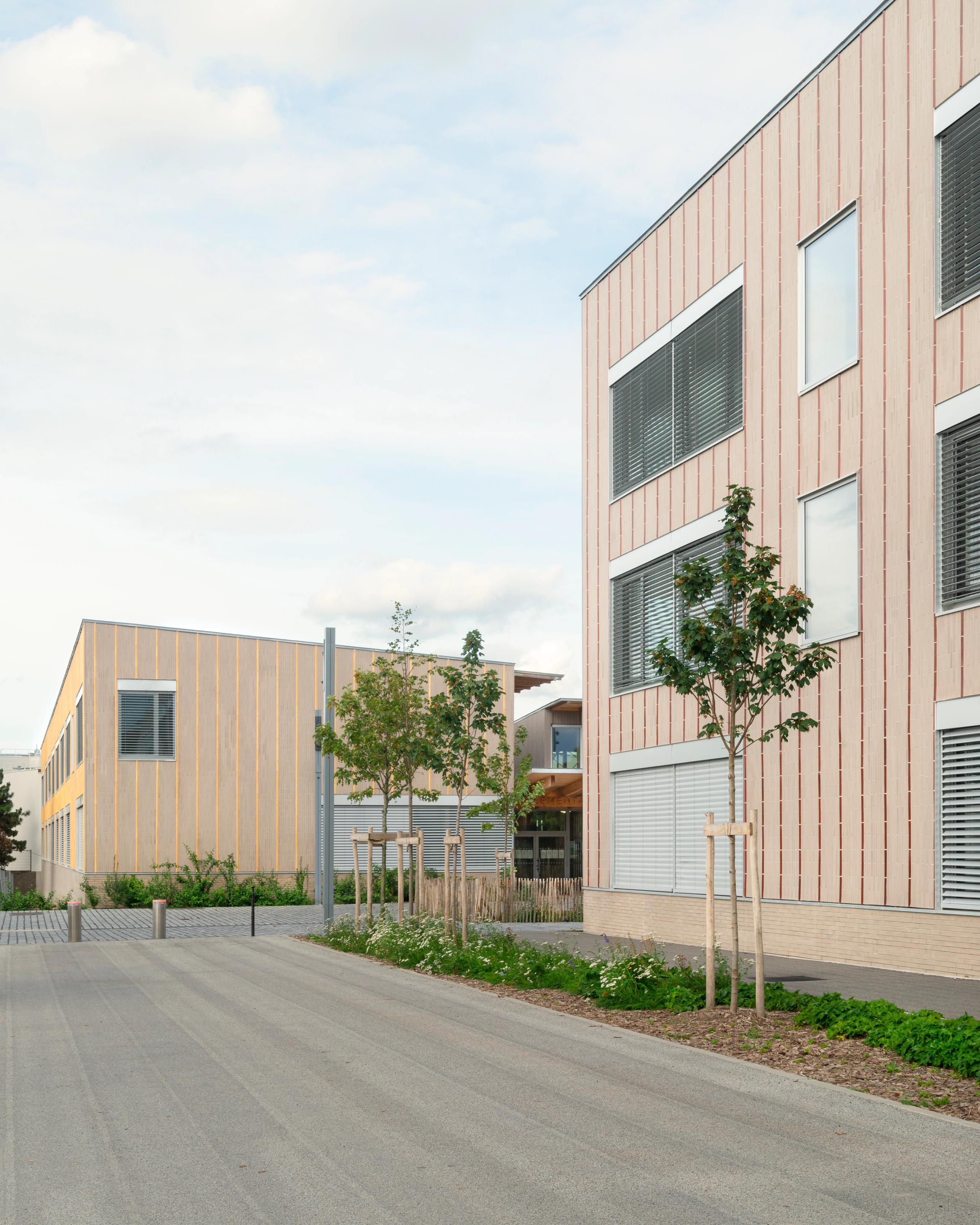 Vue des groupes scolaires Jacqueline Auriol et Jean Jaurès au Bourget : volumes en U bardés de bois clair, grandes baies à brise-soleil, parvis planté central.