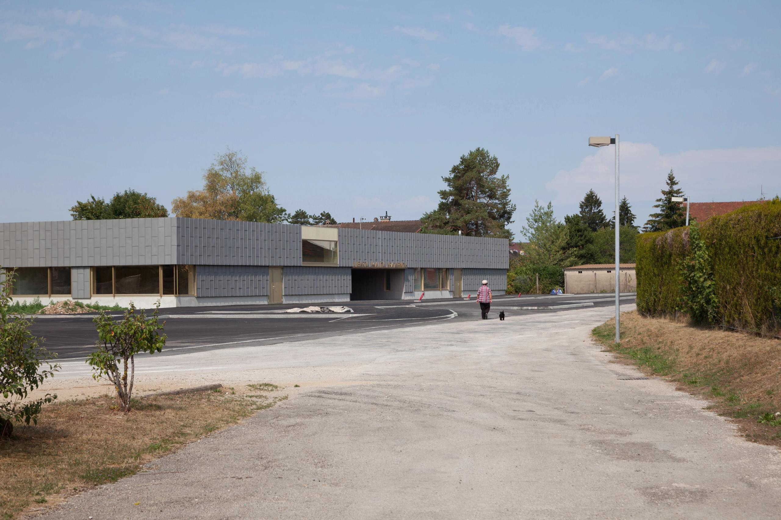 Vue extérieure de l’école élémentaire Hubert Reeves à Champagnole, volume bas en zinc à grandes baies vitrées, implanté en lisière de quartier pavillonnaire.