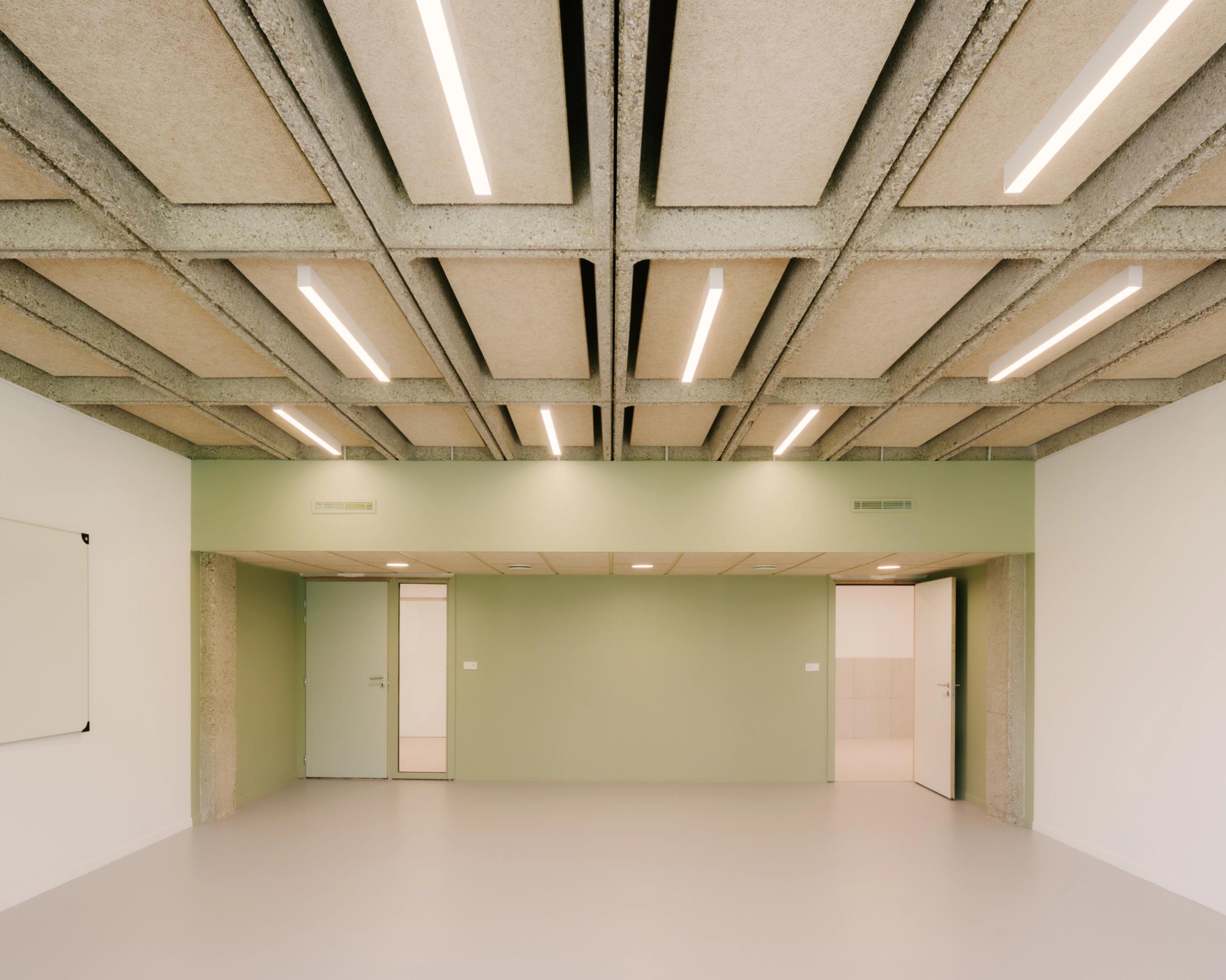 Salle rénovée du collège Maryse Bastié à Dole, montrant plancher-caisson béton apparent, éclairage linéaire et parois vert pâle dans un volume épuré.
