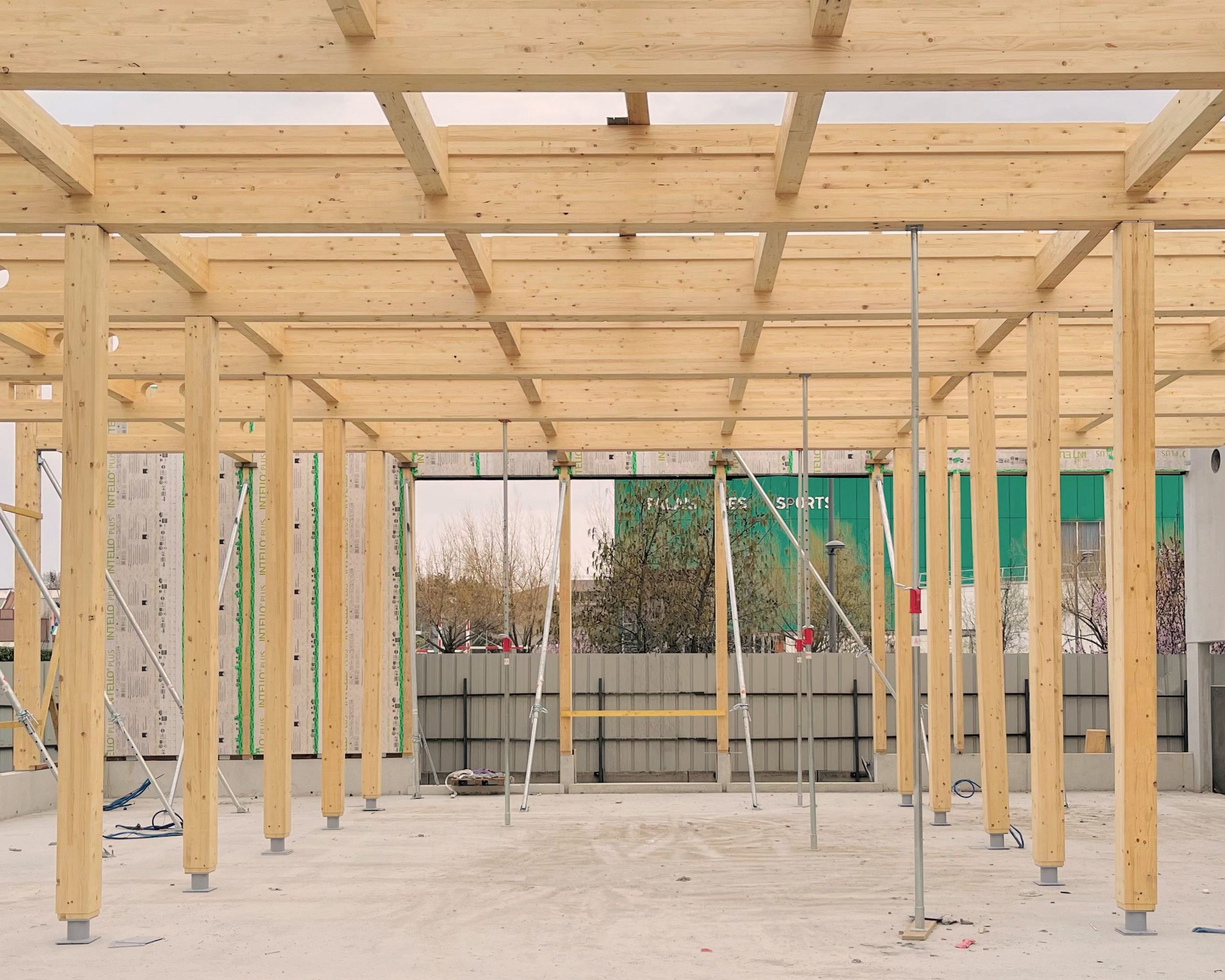 Structure en chantier de la Cité campus Assia Djebar à Vaulx-en-Velin : trame carrée de poteaux et poutres en bois lamellé sur dalle béton ouverte sur la ville.