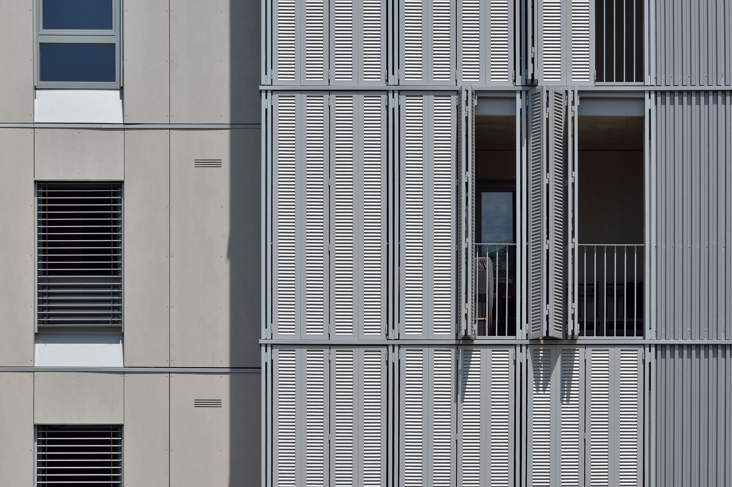 Façade des 28 logements à Villeurbanne, panneaux coulissants métalliques ajourés devant loggias et baies vitrées, alternant avec voiles en béton lisse.