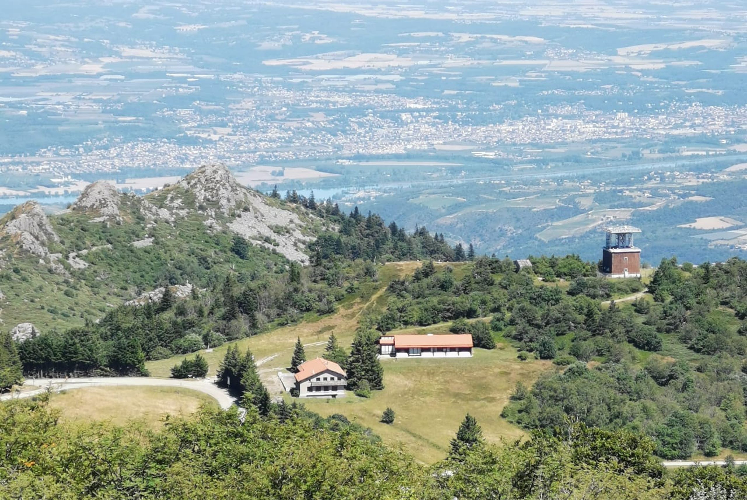Vue aérienne du col de l’Oeillon à Véranne : auberge de montagne et bâtiments annexes implantés sur un replat herbeux, ouverts sur le grand paysage vallonné.