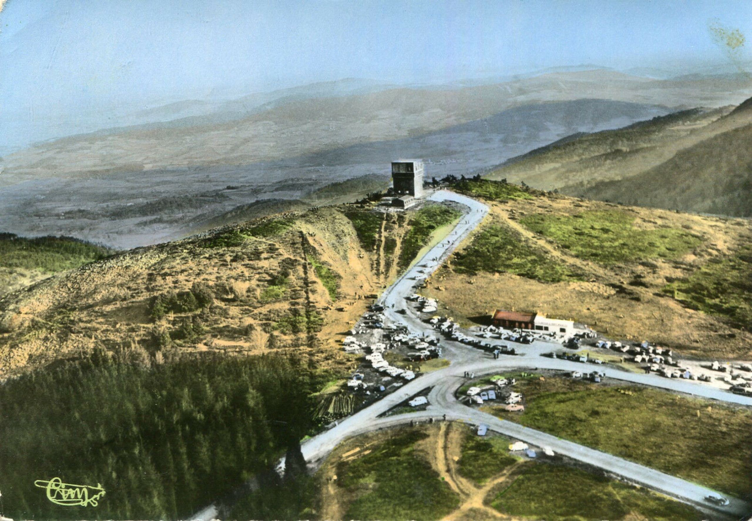 Vue aérienne du col de l’Oeillon à Véranne : ancienne auberge et bâtiments d’accueil linéaires en crête, desservis par une route sinueuse et de vastes parkings.