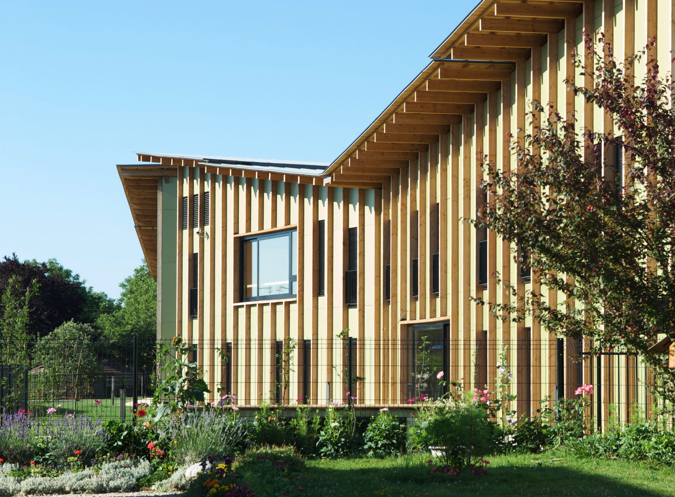 Façade bois rythmée par des montants verticaux et toiture débordante de l’EHPAD de Mervans, ouvrant sur un jardin clos paysager en premier plan.