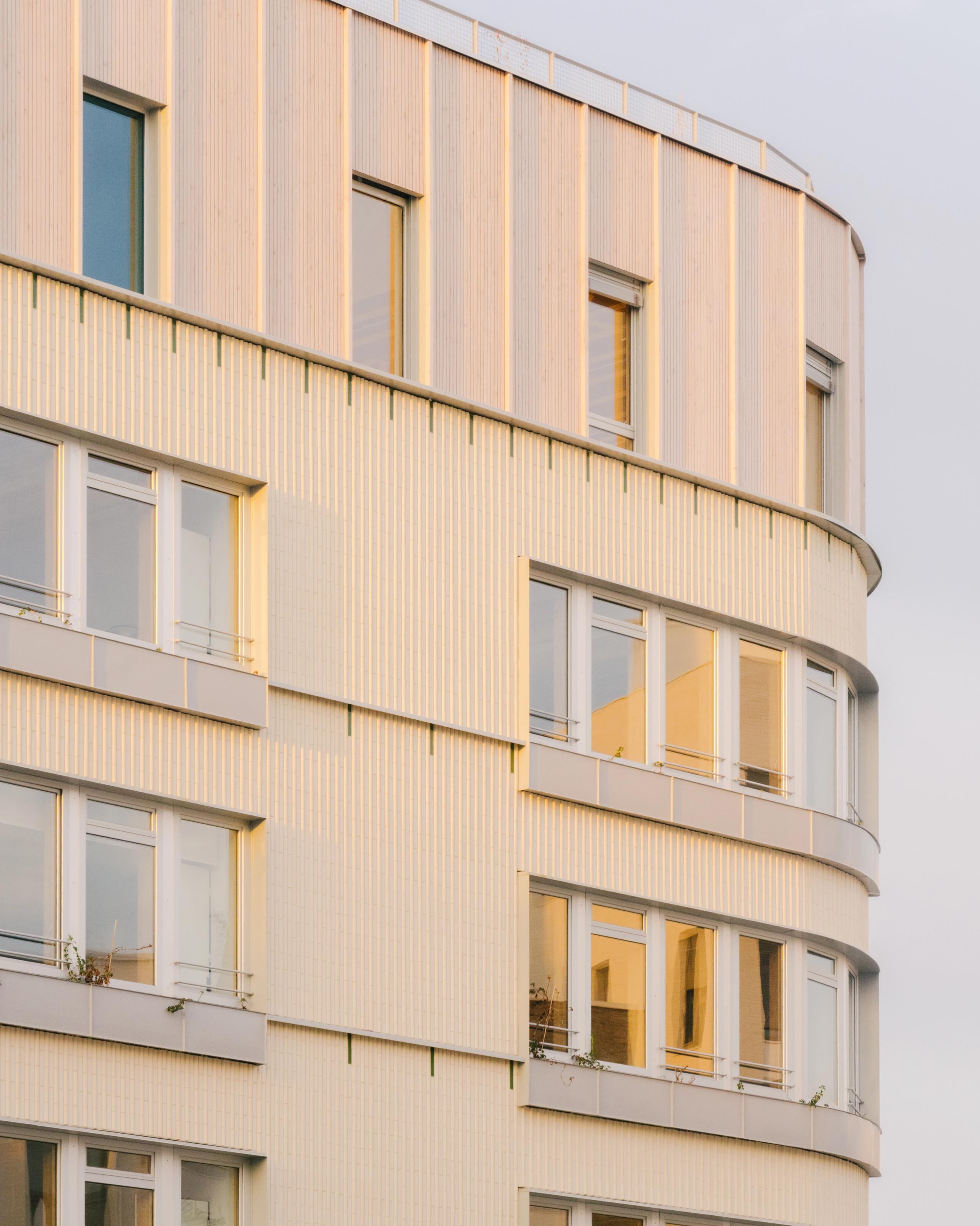 Façade du Groupe scolaire Dominique Frelaut à Colombes, volume courbe en U, bardage clair rythmé de baies vitrées et allèges métalliques en lumière rasante.