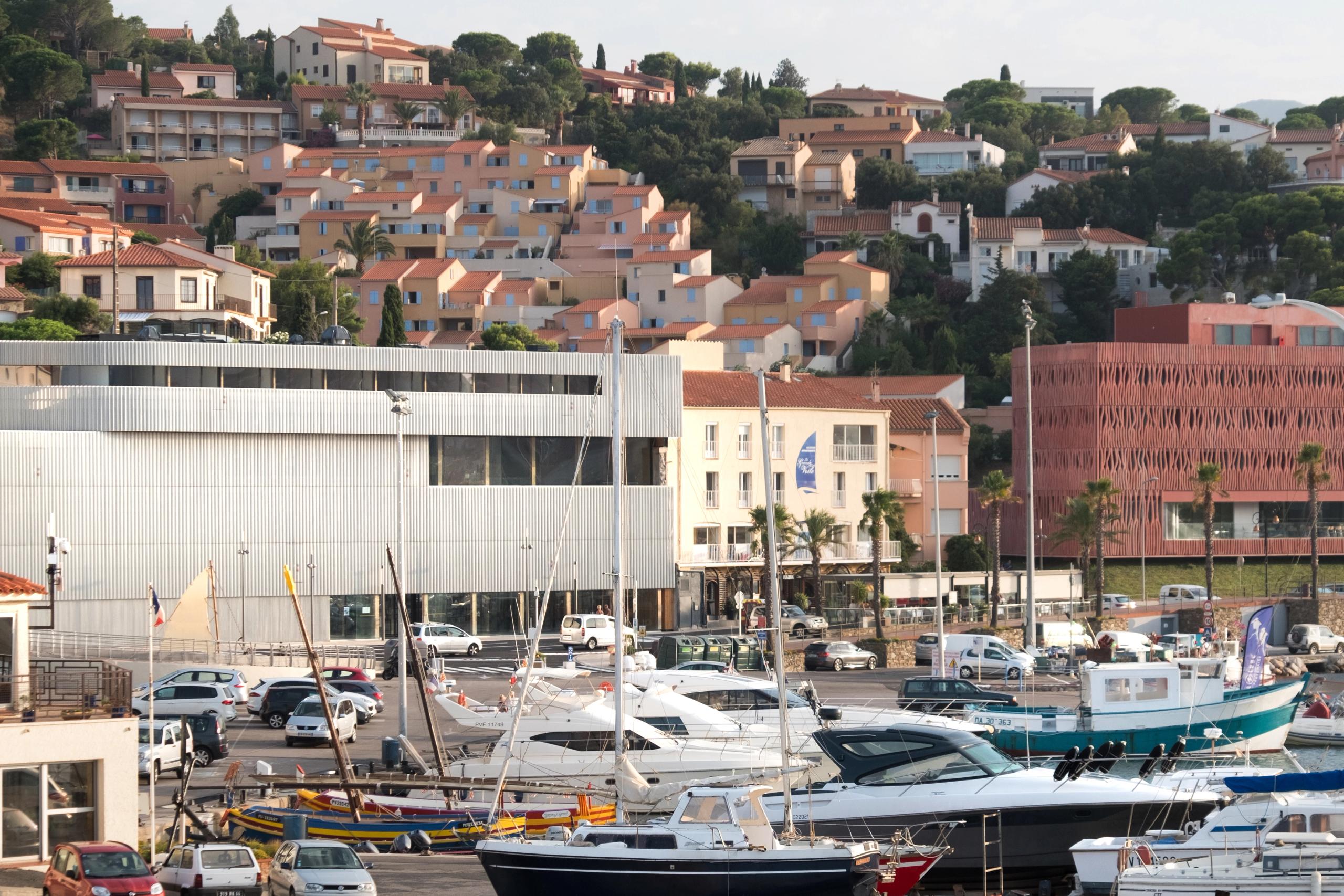 Façade horizontale métallique du Biodiversarium à Banyuls-sur-Mer, volume compact en bardage ondulé face au port, en contraste avec le tissu urbain en pente.