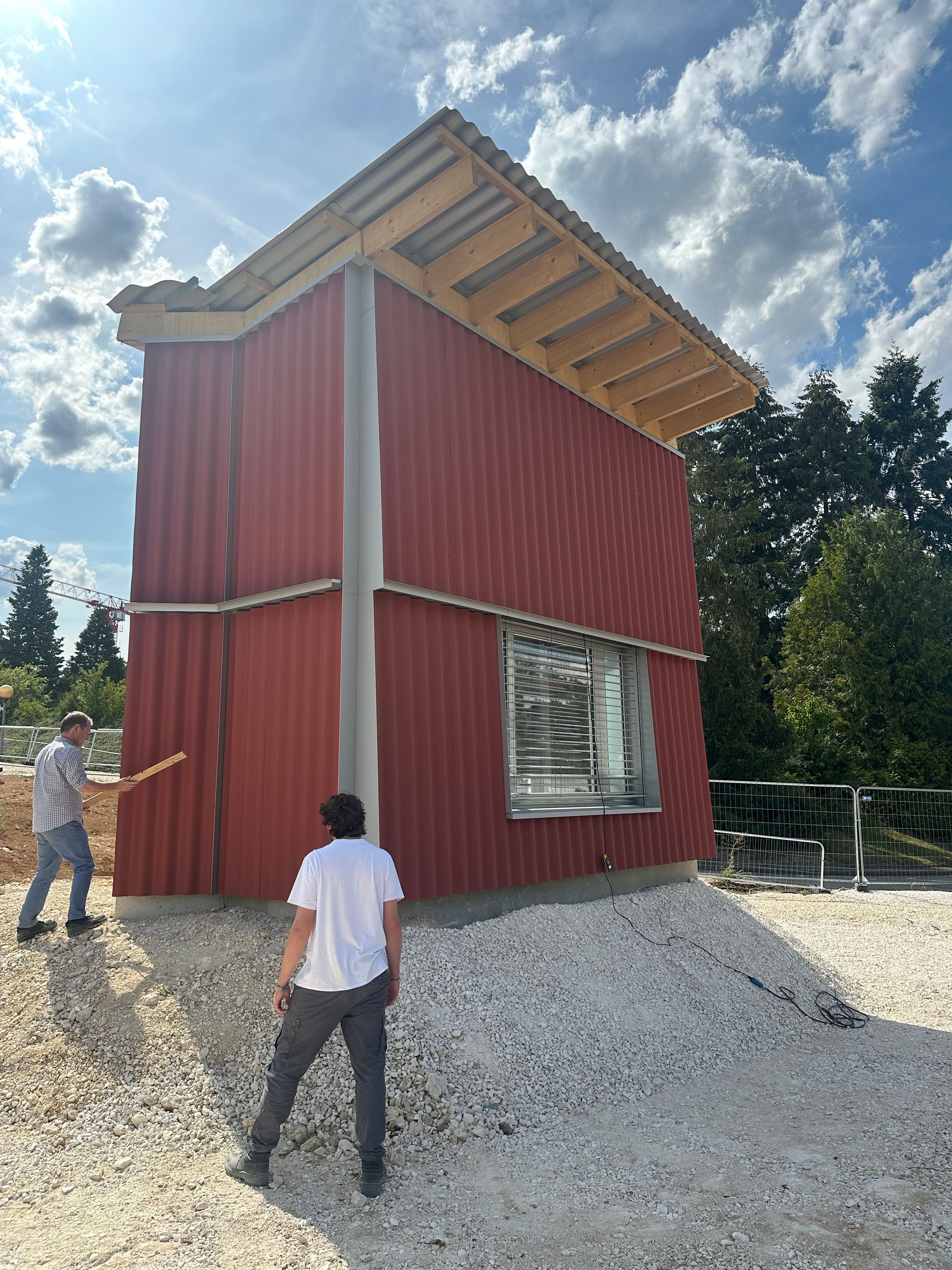 Prototype de module pour l’Ehpad d’Auxerre : volume compact en bardage métallique rouge, toiture légère en bois, posé sur plateforme de graviers en chantier.