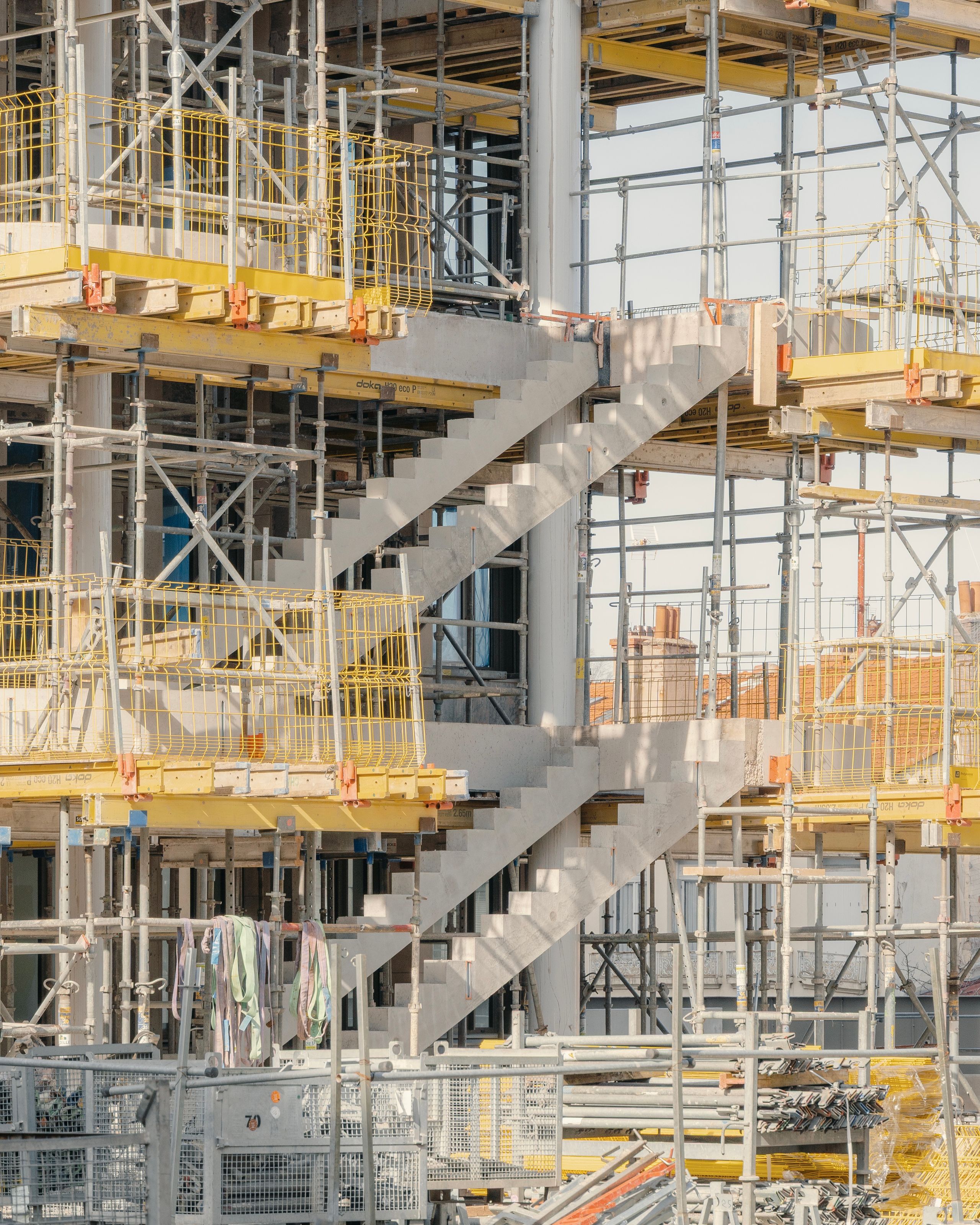 Chantier de réhabilitation de l’IGH Émile Loubet à Saint-Étienne : structure béton, escalier extérieur en cours, échafaudages métalliques et platelages provisoires.