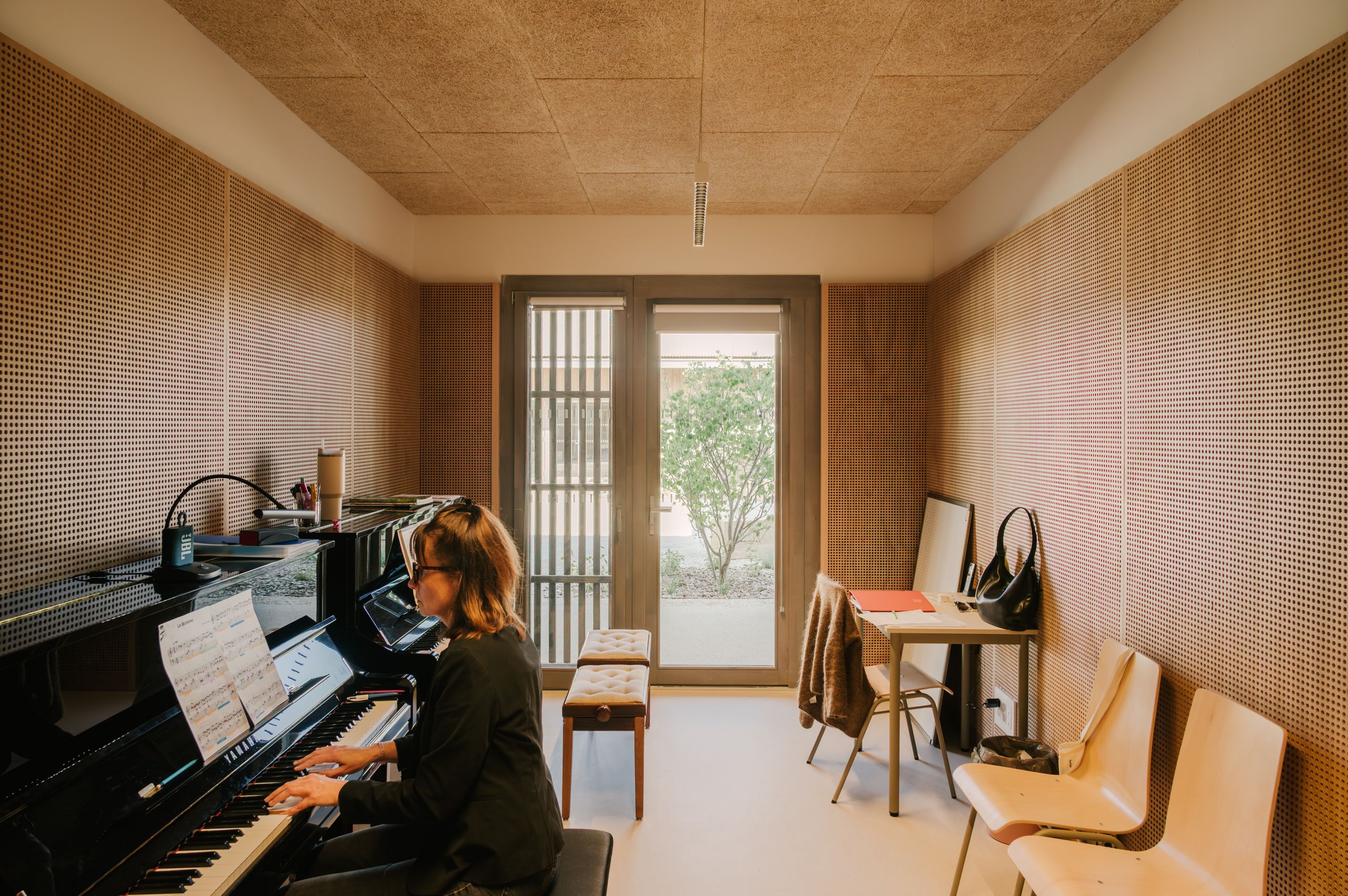 Salle de musique du pôle culture et jeunesse de Vaison-la-Romaine, aux parois acoustiques en bois perforé, ouverte par une baie vitrée sur le jardin intérieur.