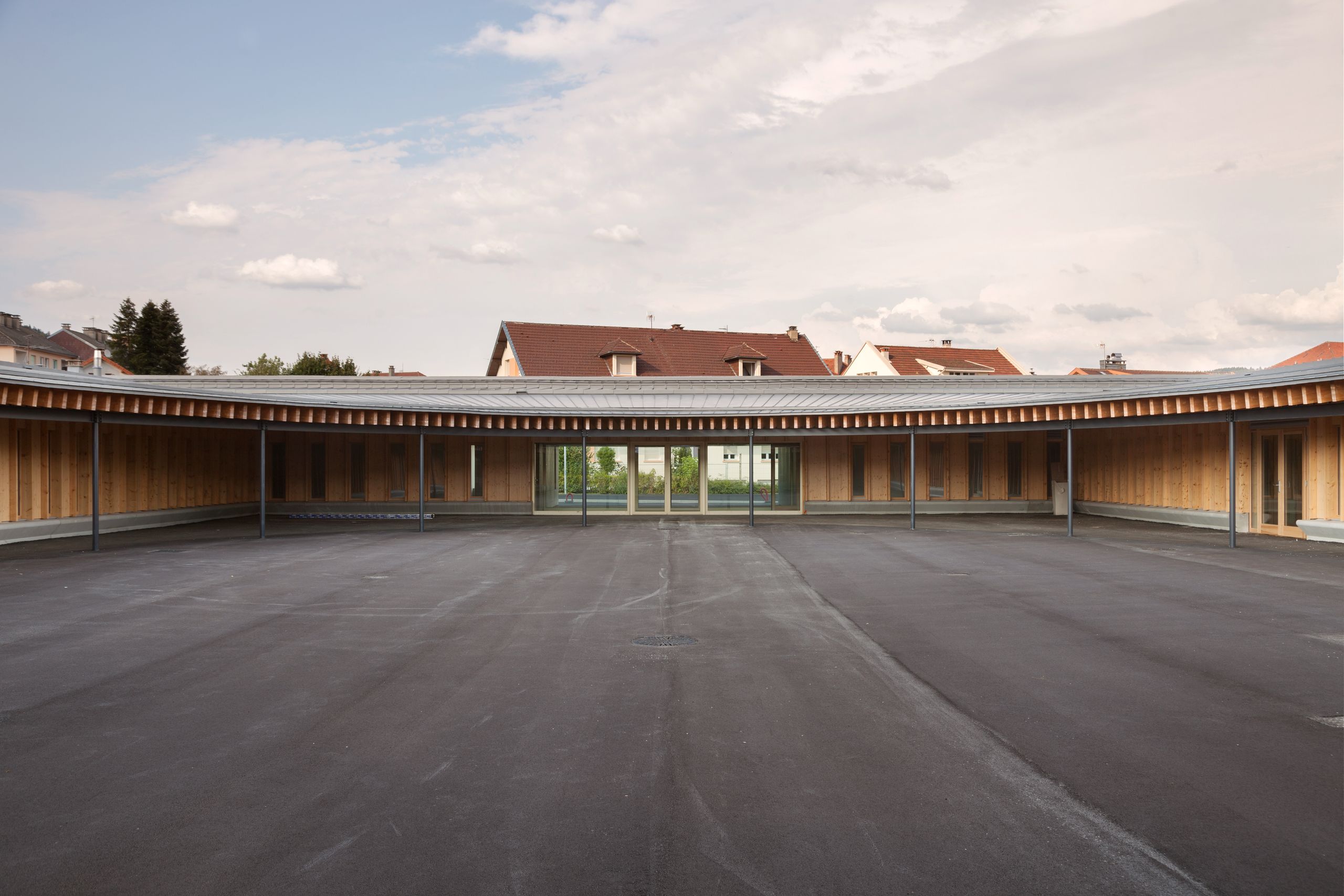 Cour centrale de l’école élémentaire Hubert Reeves à Champagnole, entourée d’un volume elliptique en ossature bois et toiture en zinc, ouverte sur le paysage.