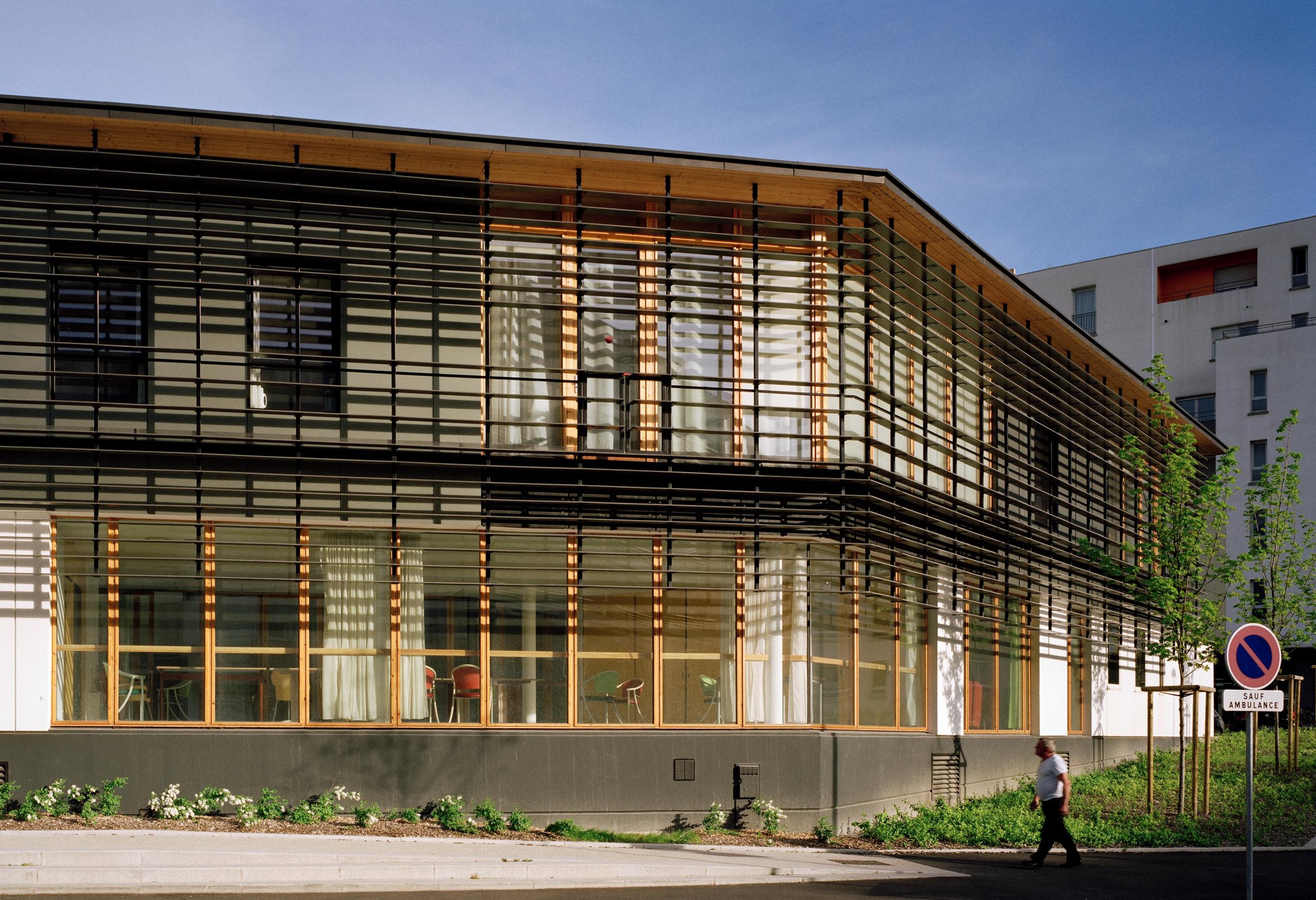 Façade de l’EHPAD à Grenoble par Tectoniques, volume R+1 vitré avec ossature bois et brise-soleil horizontaux, ouvrant sur jardins en cœur d’îlot.