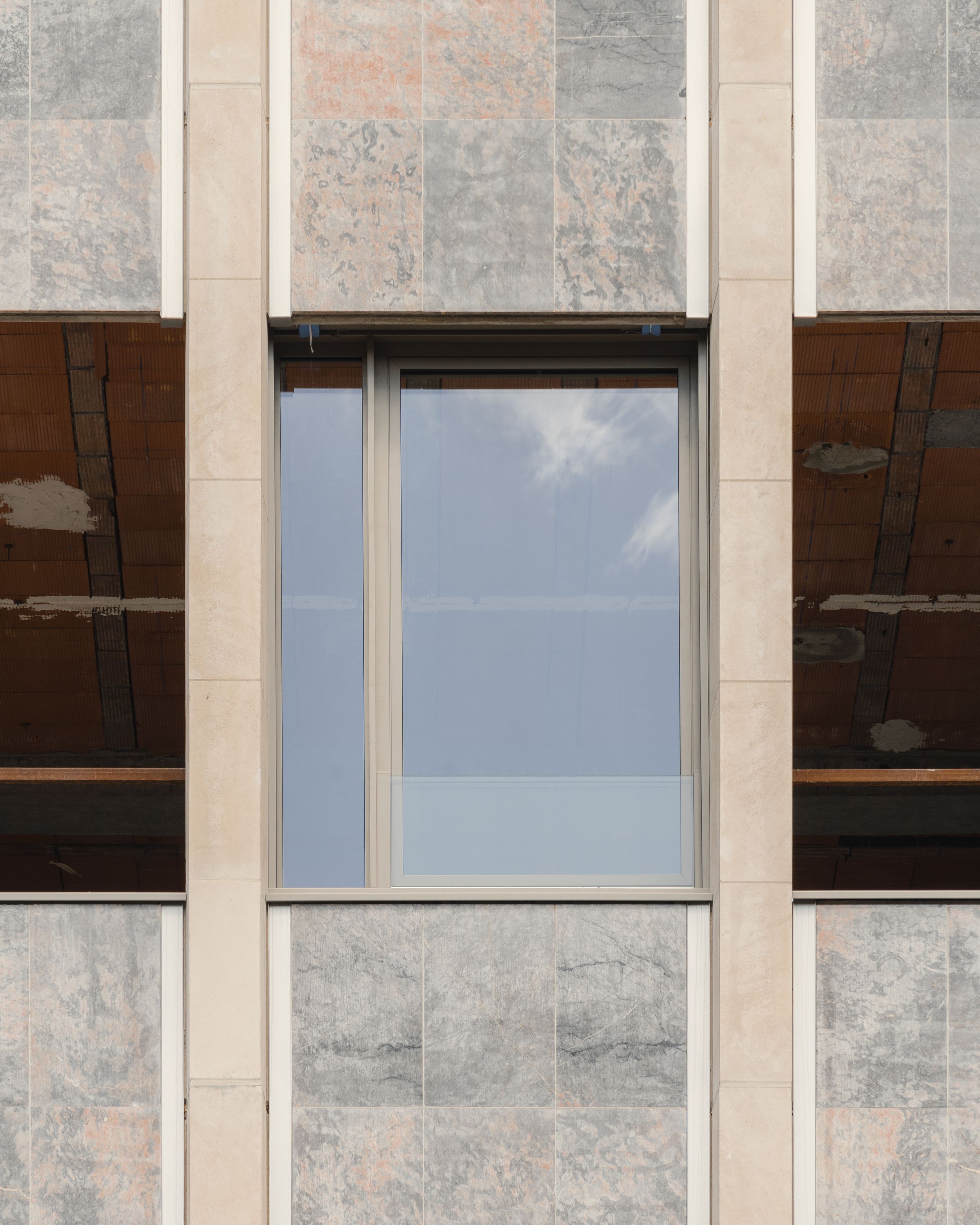Façade en chantier de l’IGH Émile Loubet à Saint-Étienne, alternant panneaux minéraux restaurés et nouvelle menuiserie vitrée encastrée dans le socle.