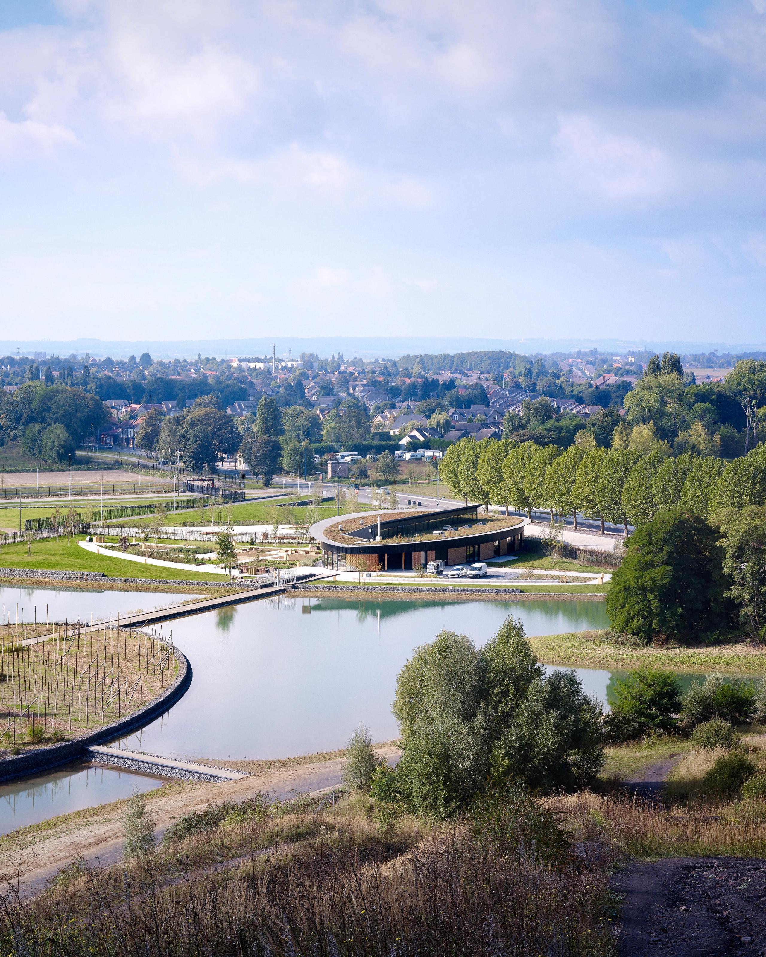 Vue aérienne du pavillon ovale de la Maison de l’environnement à Hénin-Beaumont, en ossature bois et métal, implanté au bord des plans d’eau du Parc des Îles.