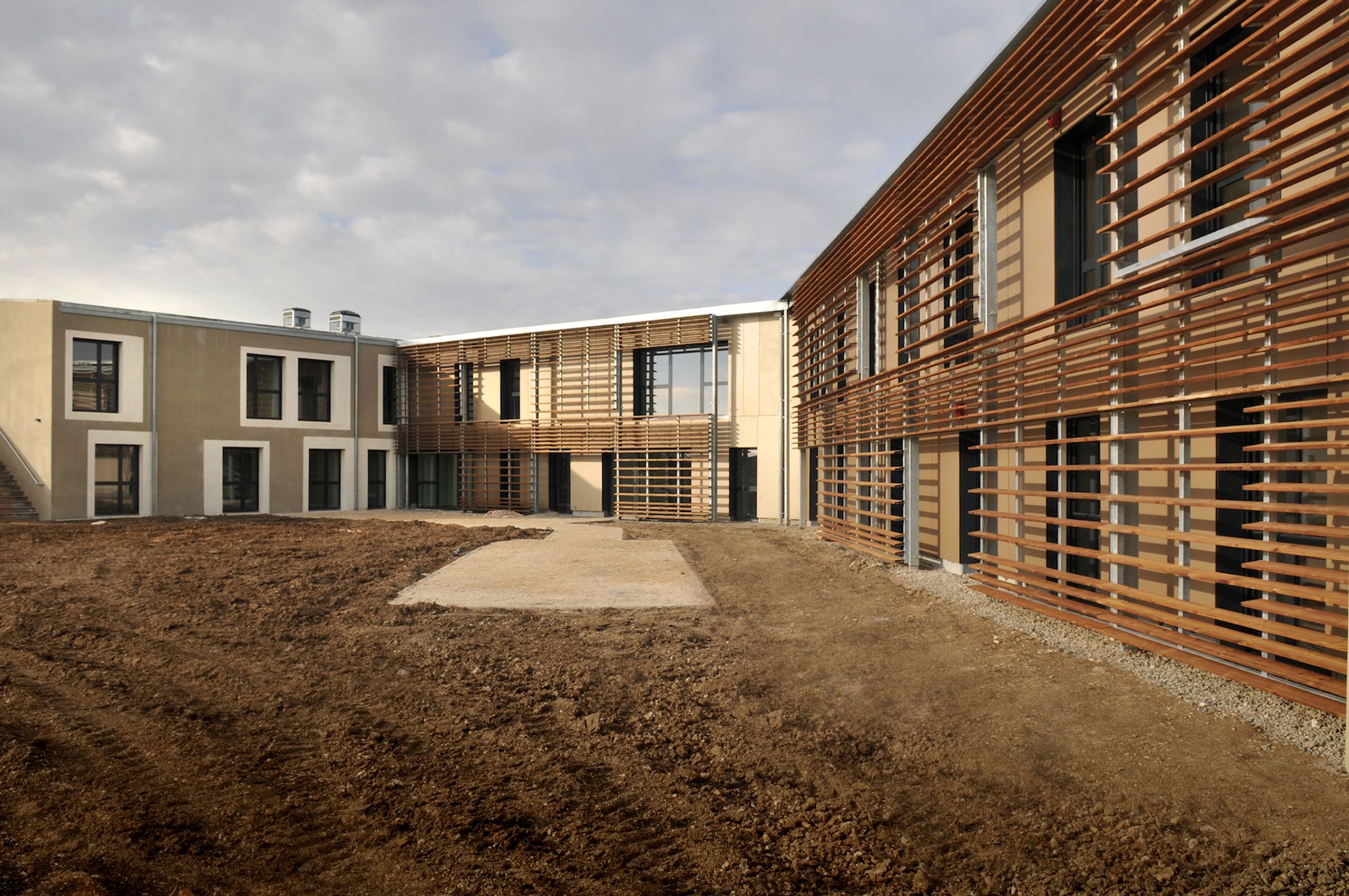 Vue de la cour de l’EHPAD de Sault par Tectoniques, bâtiment en H à deux niveaux, façades enduites rythmées par de larges baies et brise-soleil bois continus.