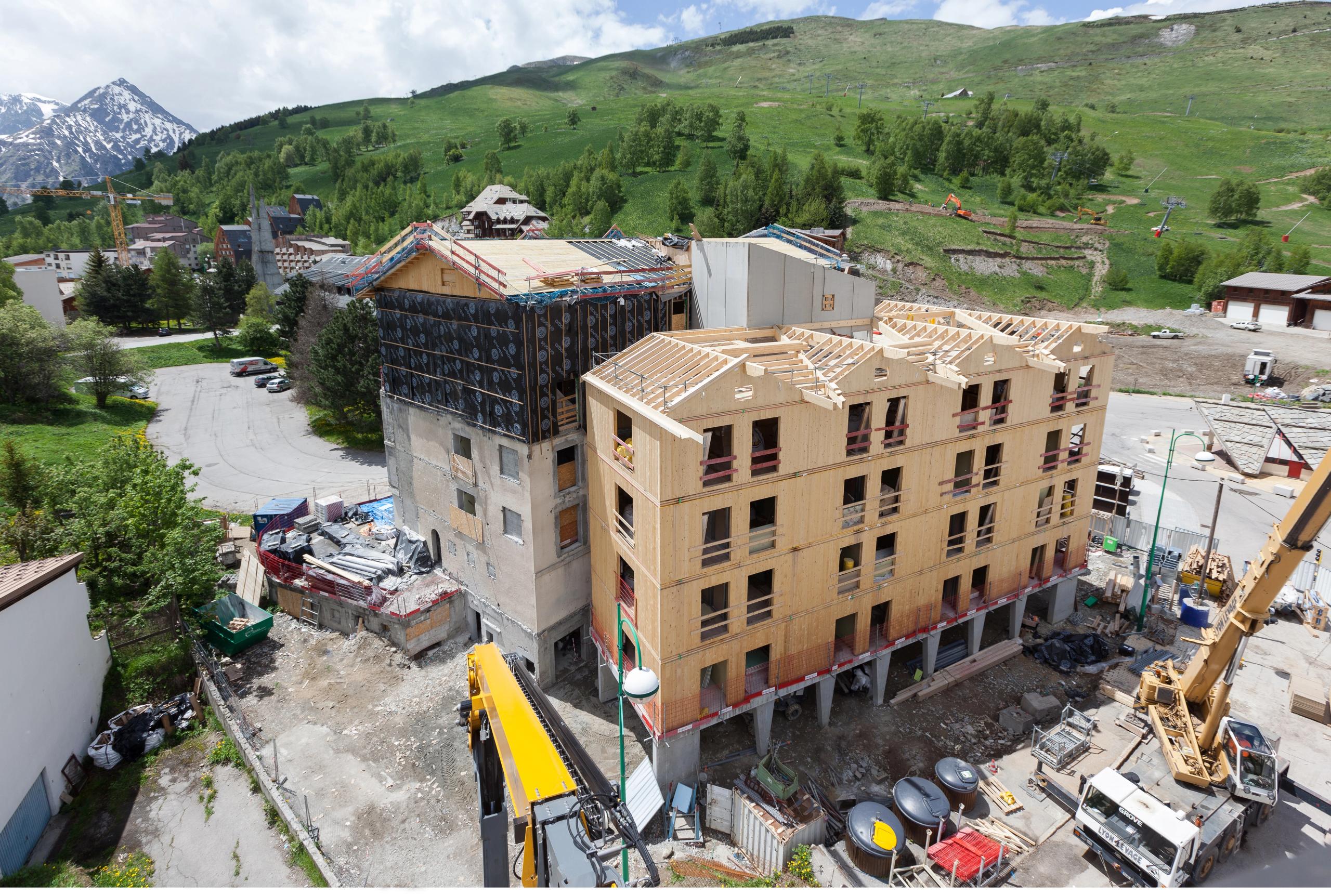 Chantier de réhabilitation et extension de l’auberge de jeunesse aux Deux Alpes, structure mixte béton–CLT surélevée, toitures à deux pans en site alpin.