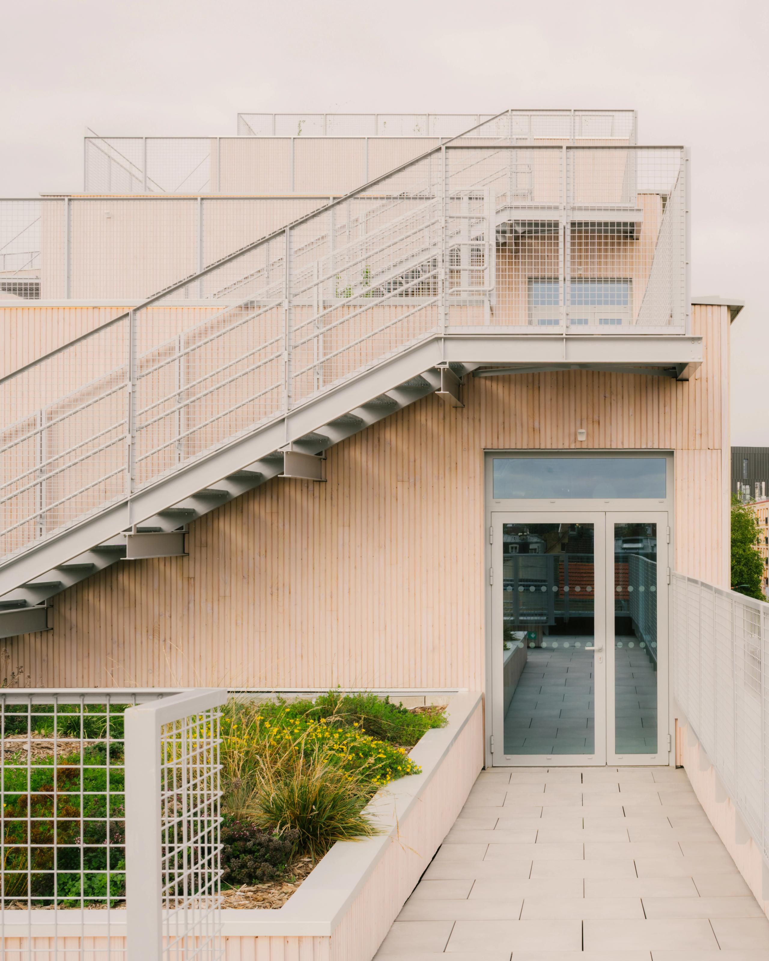 Terrasse-jardin du Groupe scolaire Dominique Frelaut à Colombes, façade en bois claire, escalier métallique extérieur et circulations en toiture.