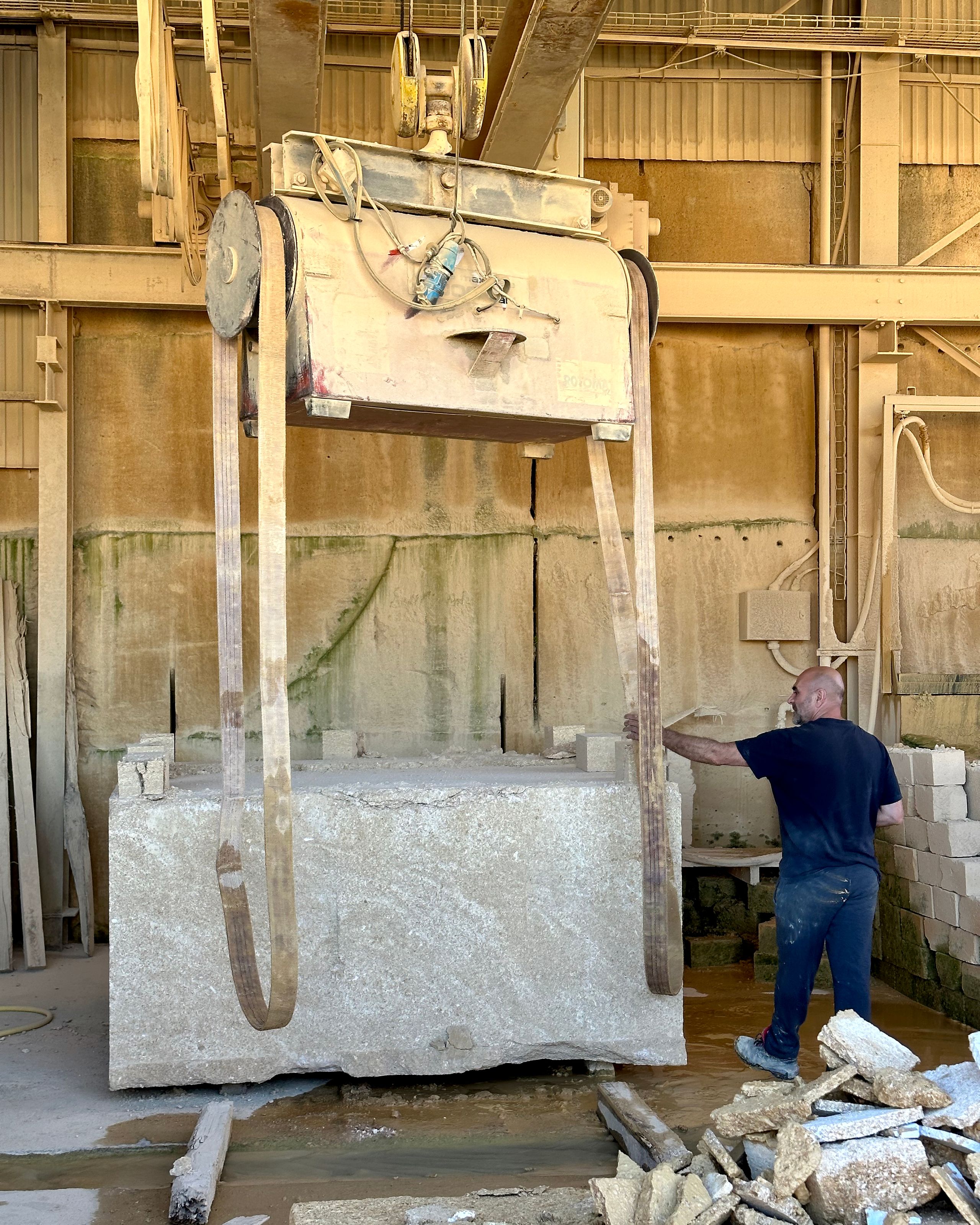 Bloc de pierre massive pour le pôle culture et jeunesse de Vaison-la-Romaine, manutentionné en carrière par un pont roulant dans un atelier industriel.