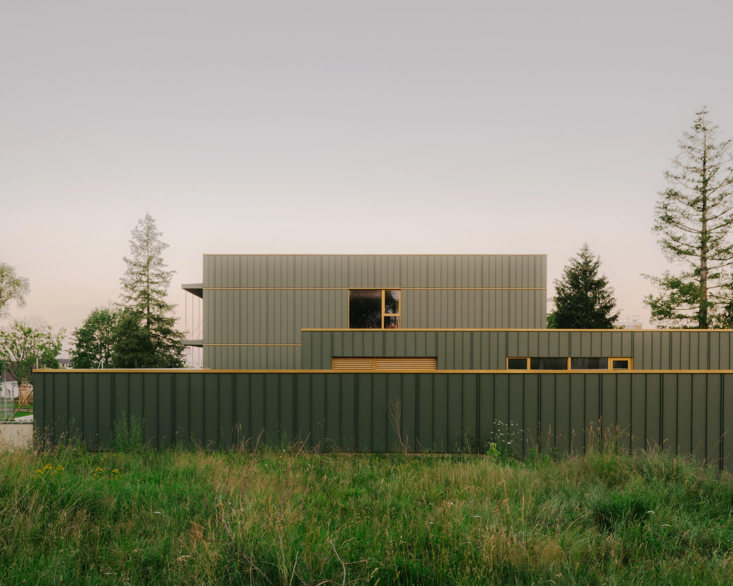 Façade restructurée du collège Maryse Bastié à Dole : volumes superposés en bardage métallique vert, trame rationnelle et ouvertures cadrées sur un terrain végétalisé.