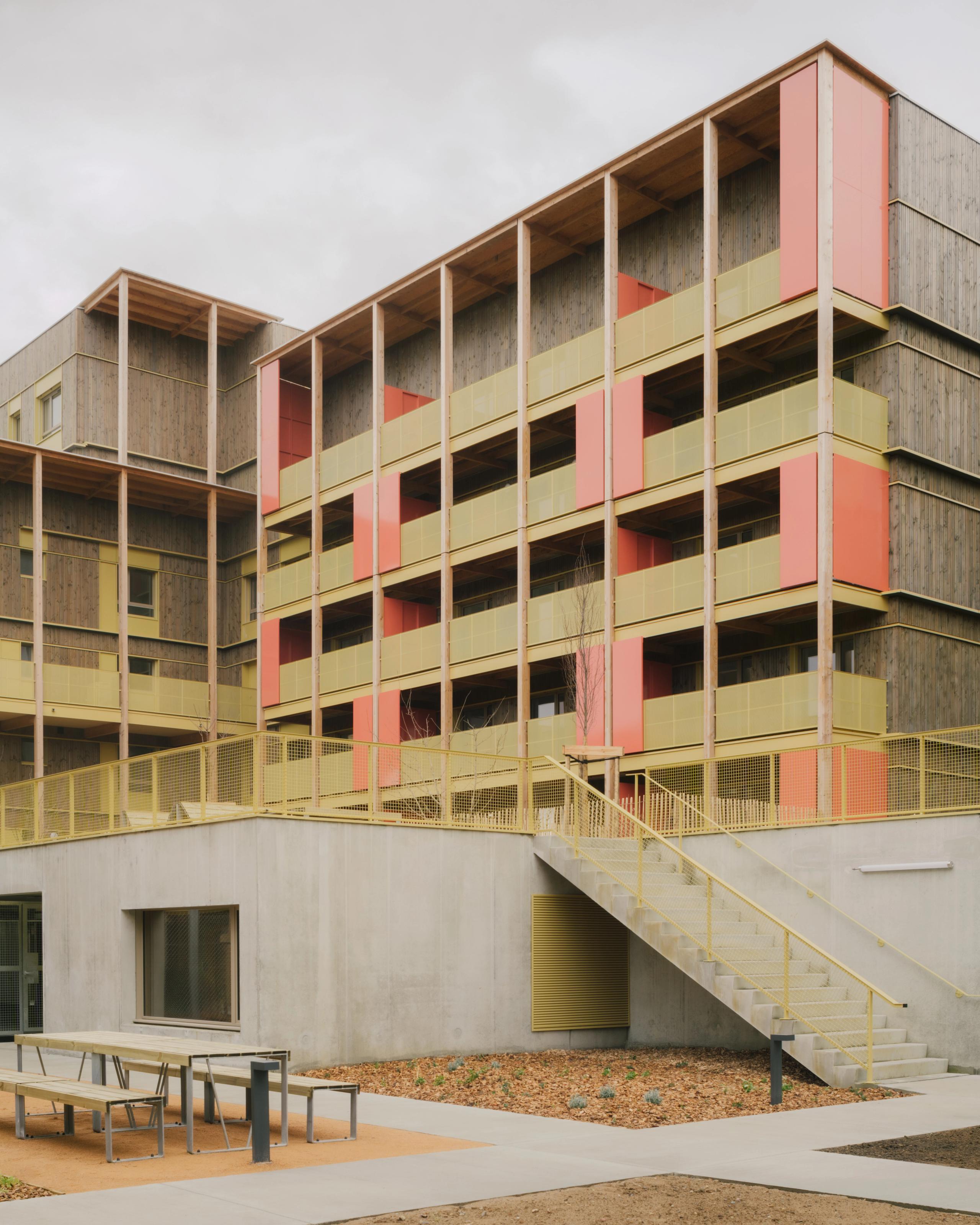 Livraison des 84 logements à Trévoux par Tectoniques : volumes en gradins bois-béton, coursives extérieures, exo-structures bois et garde-corps colorés.