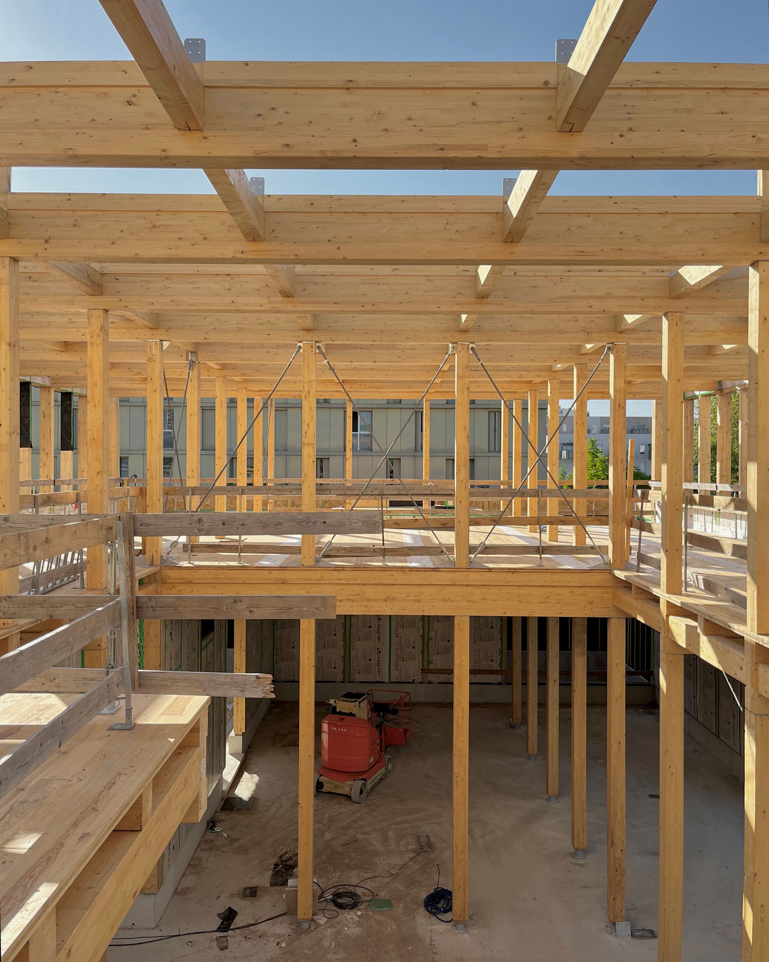 Structure bois en cours de chantier de la Cité campus Assia Djebar à Vaulx-en-Velin, charpente en poutres tissées formant trame carrée sur double hauteur.