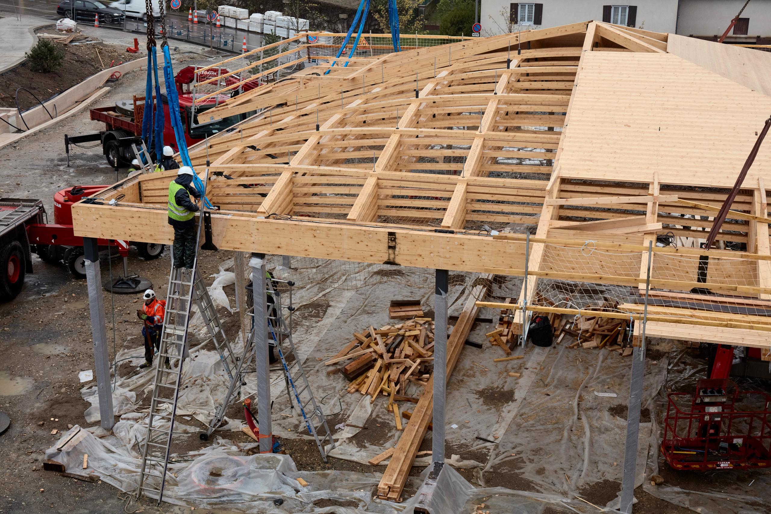 Chantier de la halle de marché de Marcy-l’Étoile : levage de la charpente bois lamellé-collé sur poteaux métalliques, toiture carrée en cours d’assemblage.