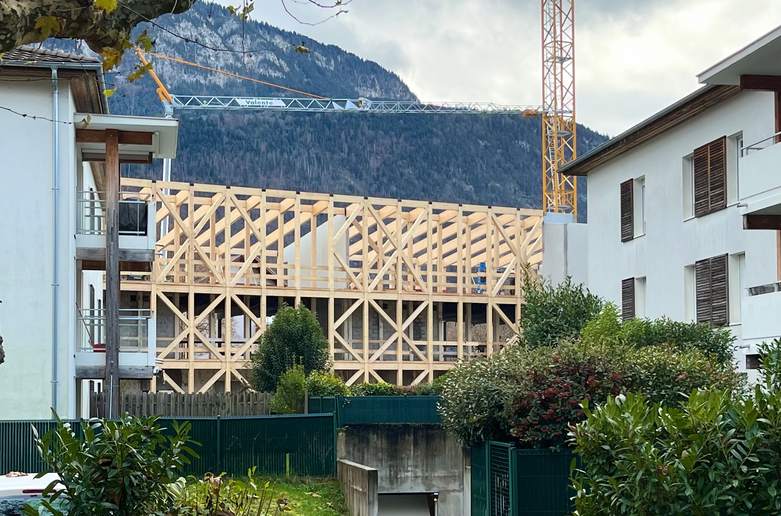 Chantier du groupe scolaire du Bouchet à Bonneville : surélévation en ossature bois apparente sur structure béton existante, avec grue et massif montagneux en arrière-plan.