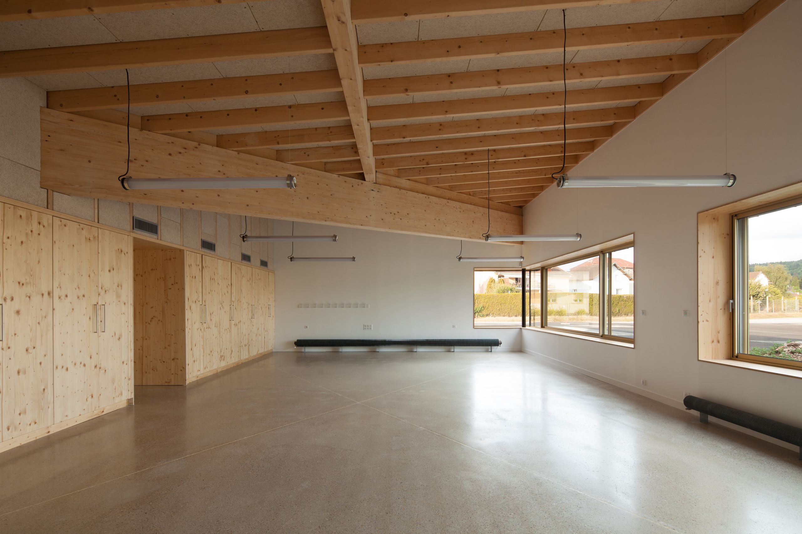 Intérieur d’une salle de l’école élémentaire Hubert Reeves à Champagnole, ossature bois apparente, grands rangements intégrés et larges baies vitrées sur le paysage.