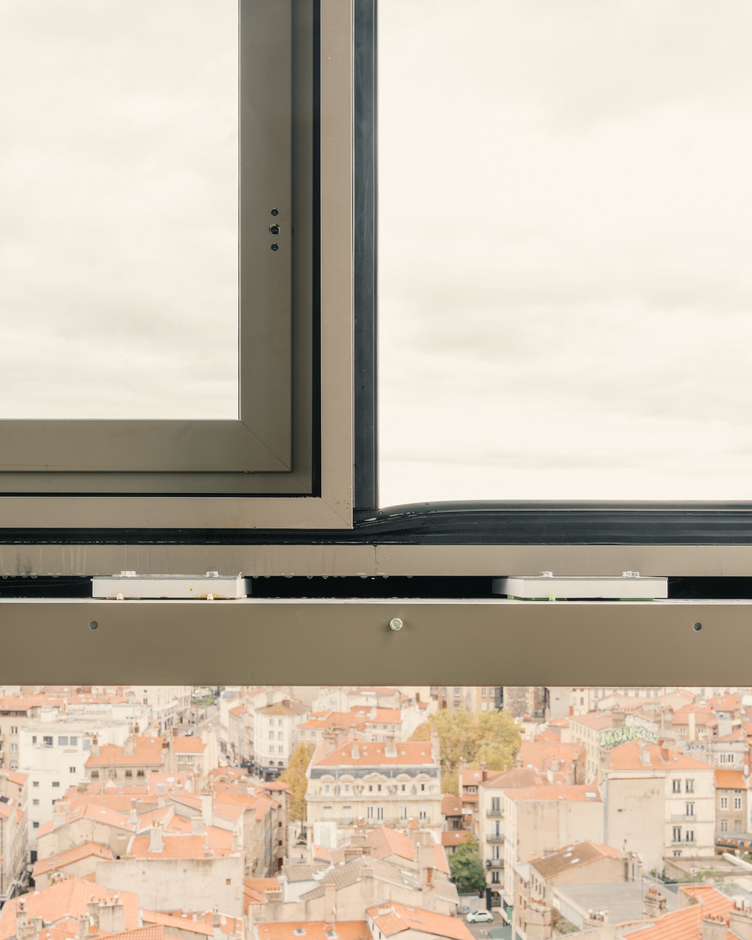 Détail de façade vitrée de l’IGH Émile Loubet à Saint-Étienne, châssis aluminium rénové en premier plan, vue plongeante sur les toitures de la ville.