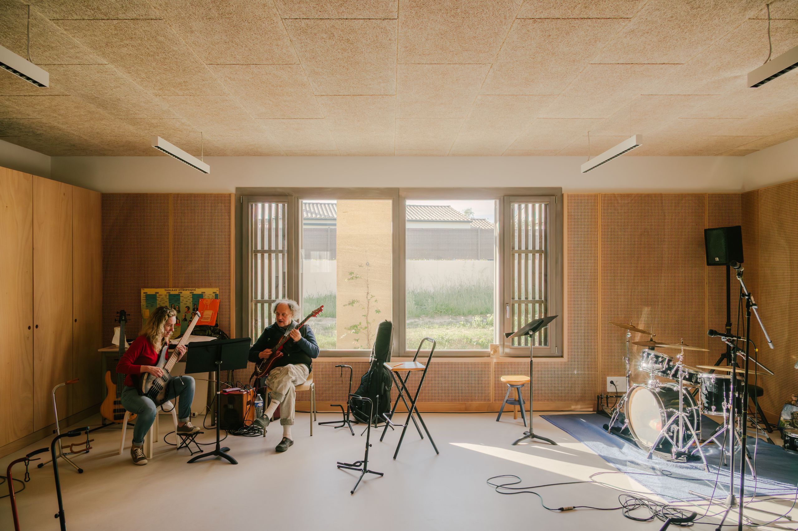 Salle de musique du pôle culture et jeunesse de Vaison-la-Romaine, aux parois bois et plafond acoustique, largement éclairée par une baie vitrée sur jardin.