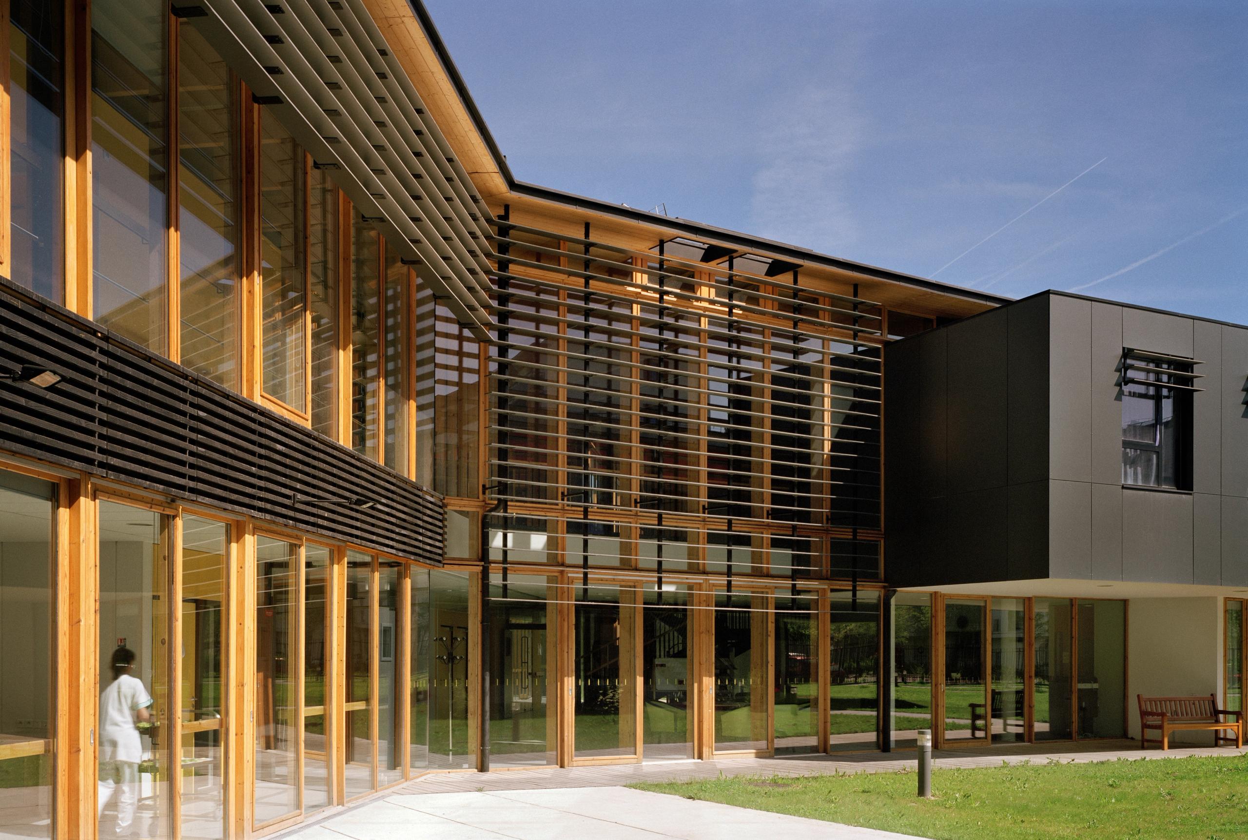 Façade de l’EHPAD à Grenoble par Tectoniques, volumes bois-verre à deux niveaux, brise-soleil horizontaux et larges baies vitrées ouvrant sur les jardins.