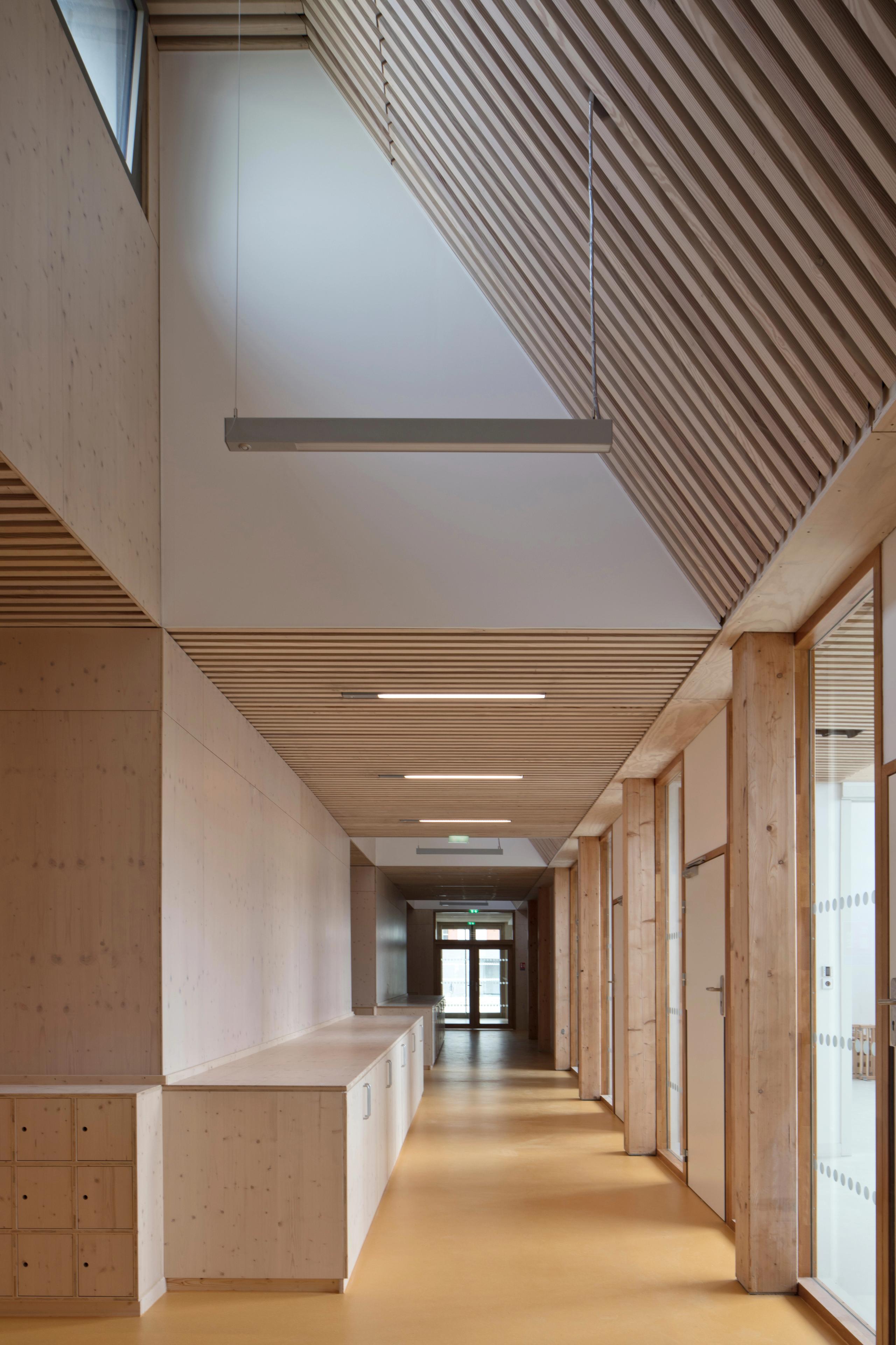 Couloir du groupe scolaire Denis Mukwege à Melun, structure bois apparente, plafond à lames, lumière naturelle latérale et mobilier intégré en second œuvre bois.