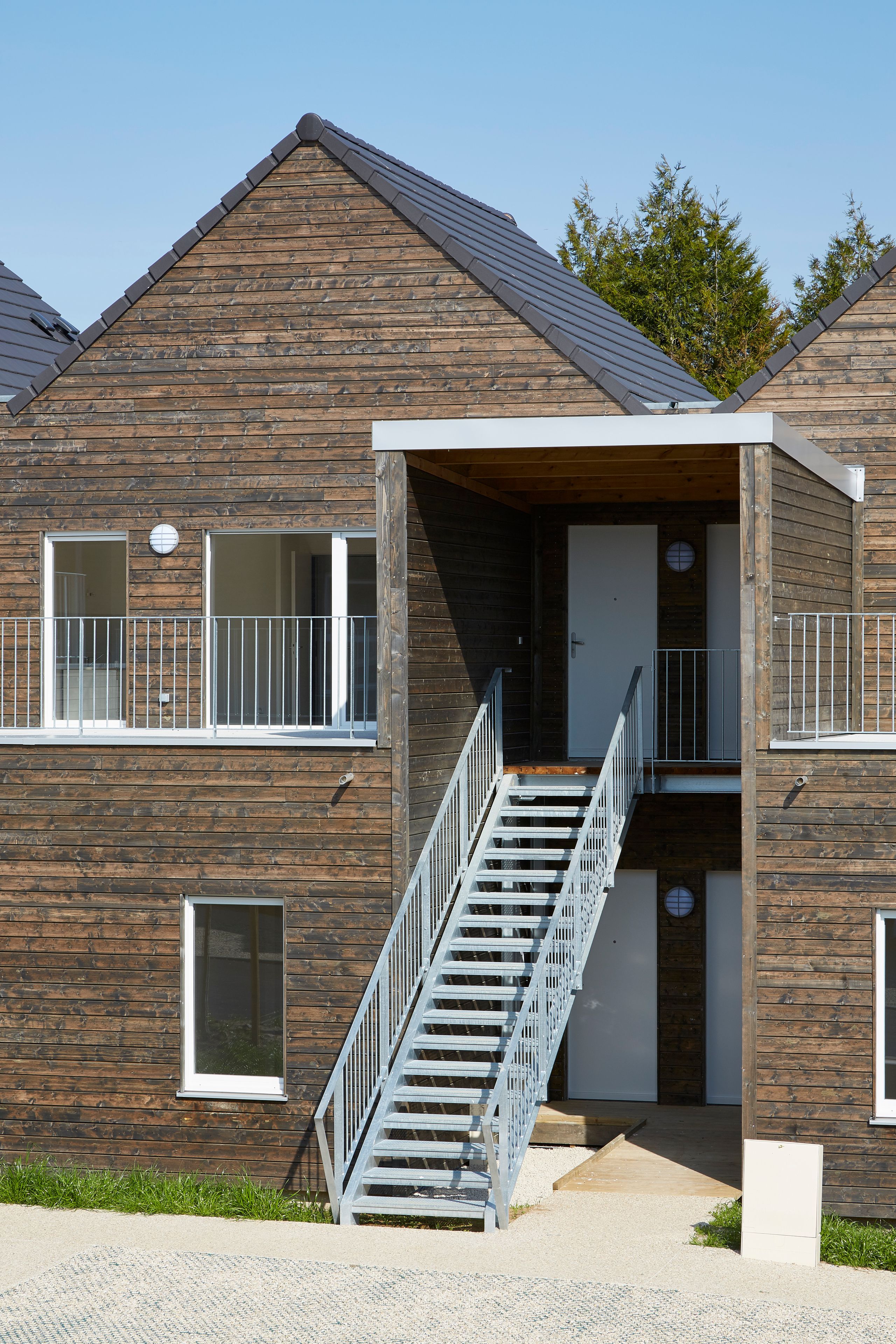 Façade en bardage bois des 36 logements à Vauhallan par Tectoniques, avec escalier métallique extérieur, coursives et toitures à deux pans alignées.